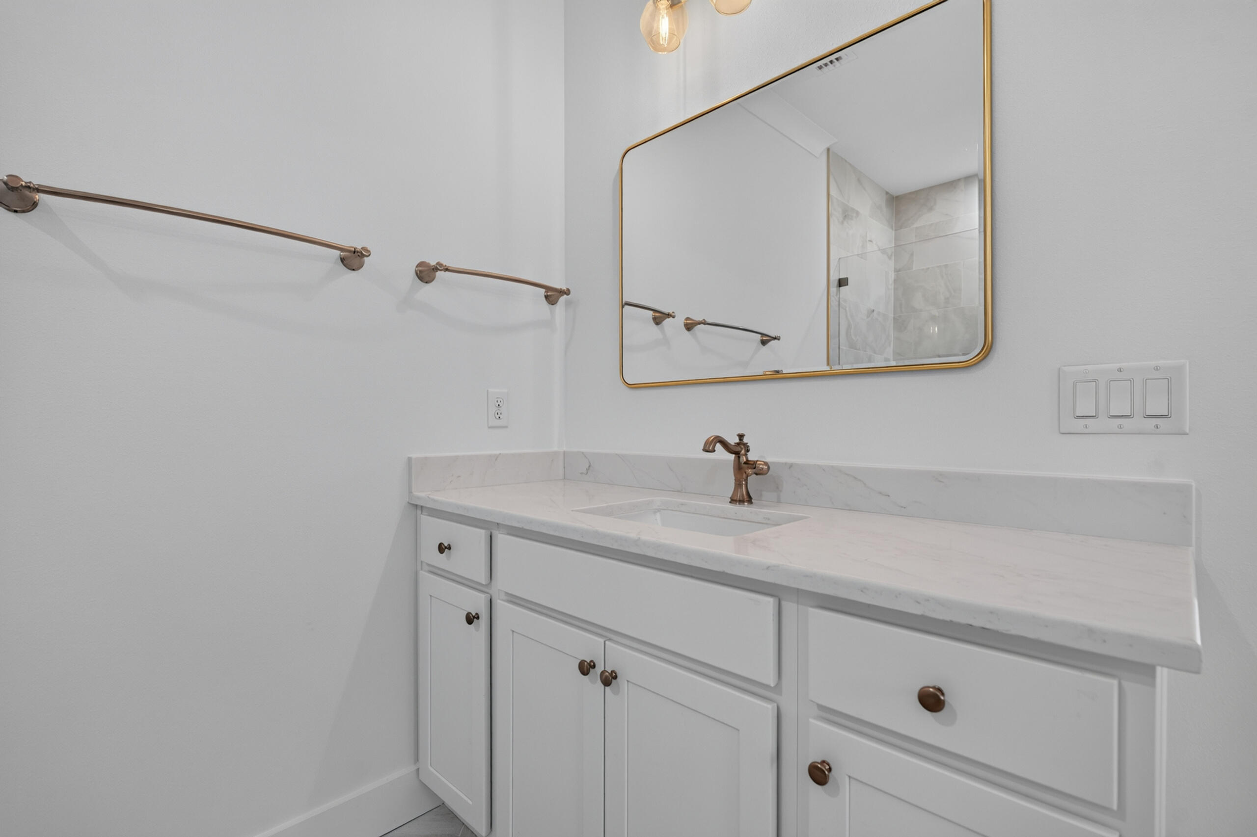 Bathroom vanity with white cabinets, marble-look counter, bronze fixtures, and gold-framed mirror.