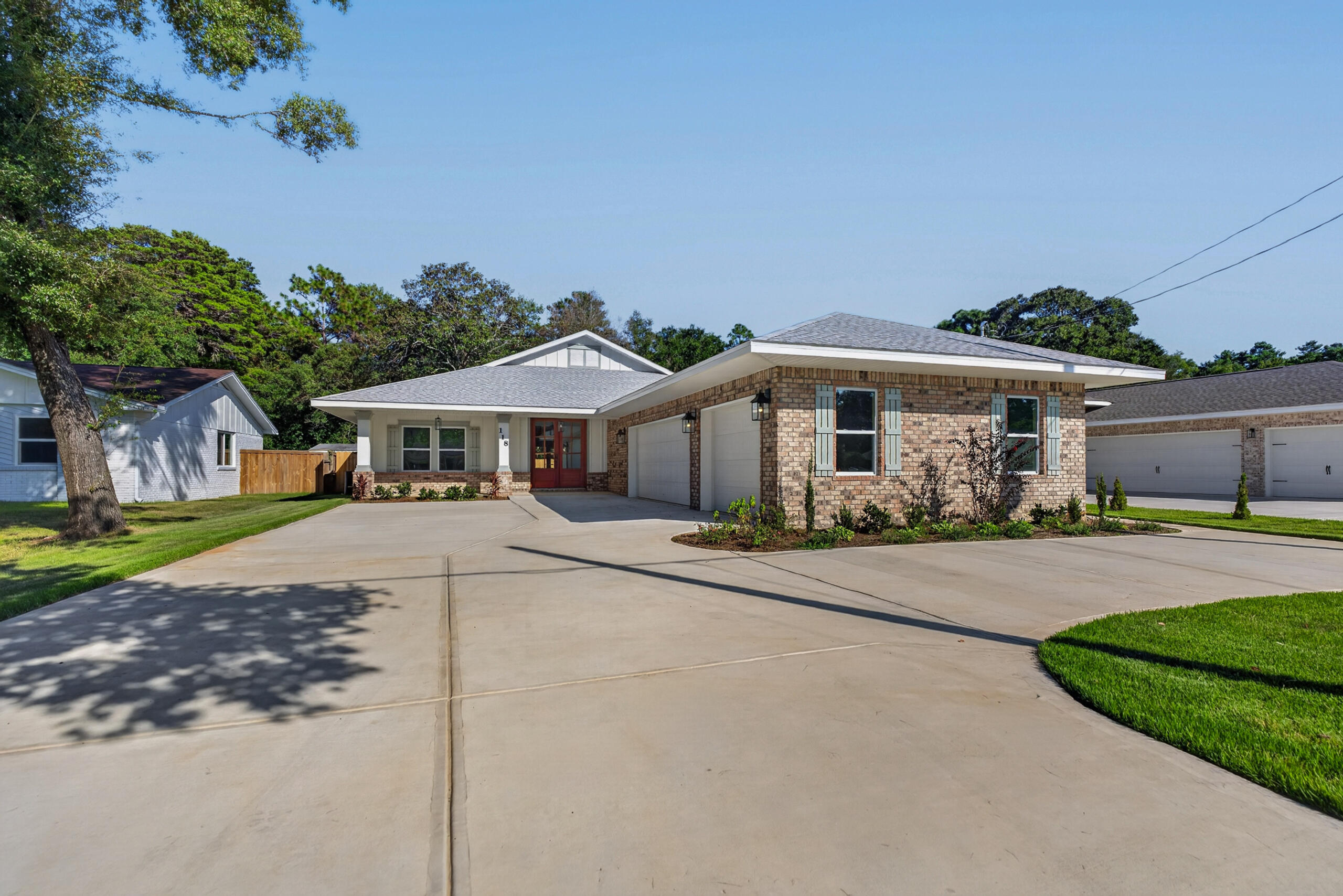 Single-story brick home with a red front door, attached garage, and broad concrete driveway.