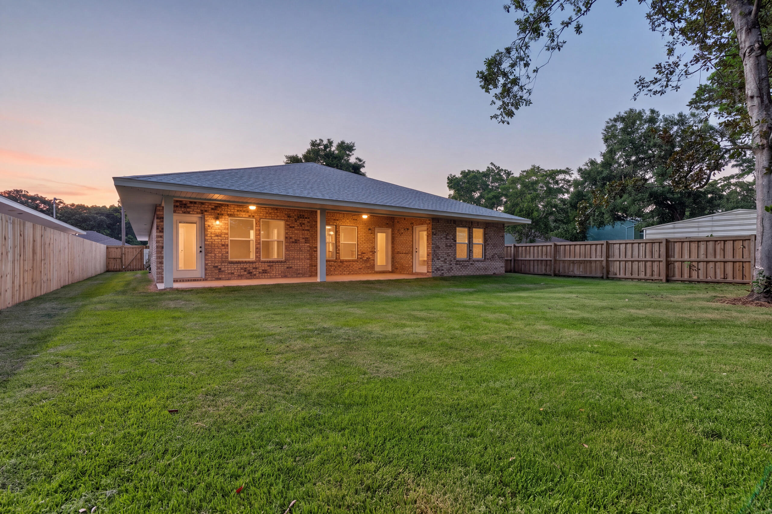 Brick house with a covered patio and fenced lawn at dusk