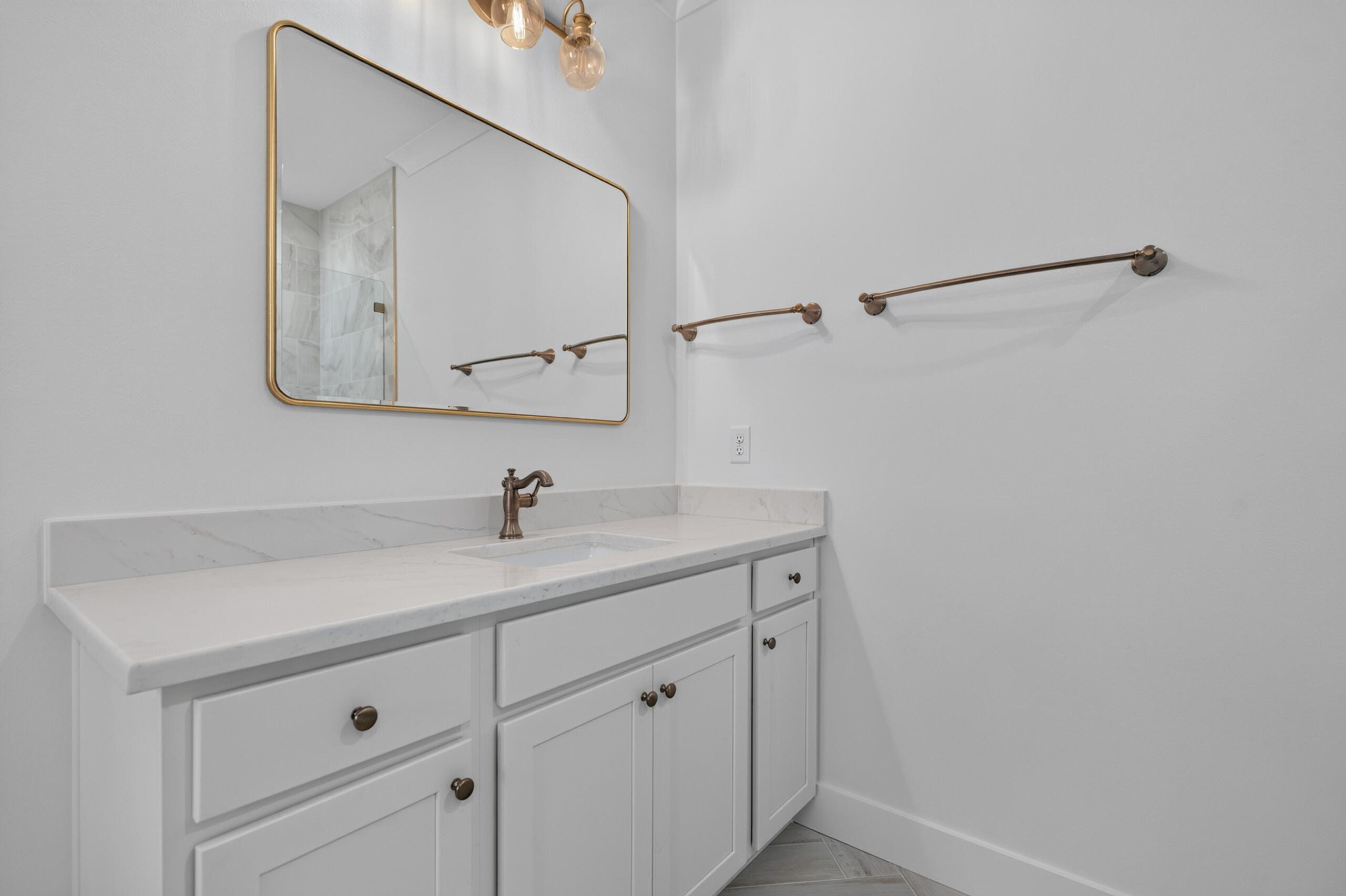 Bathroom vanity with a gold-framed mirror, marble-look counter, and bronze-tone fixtures.