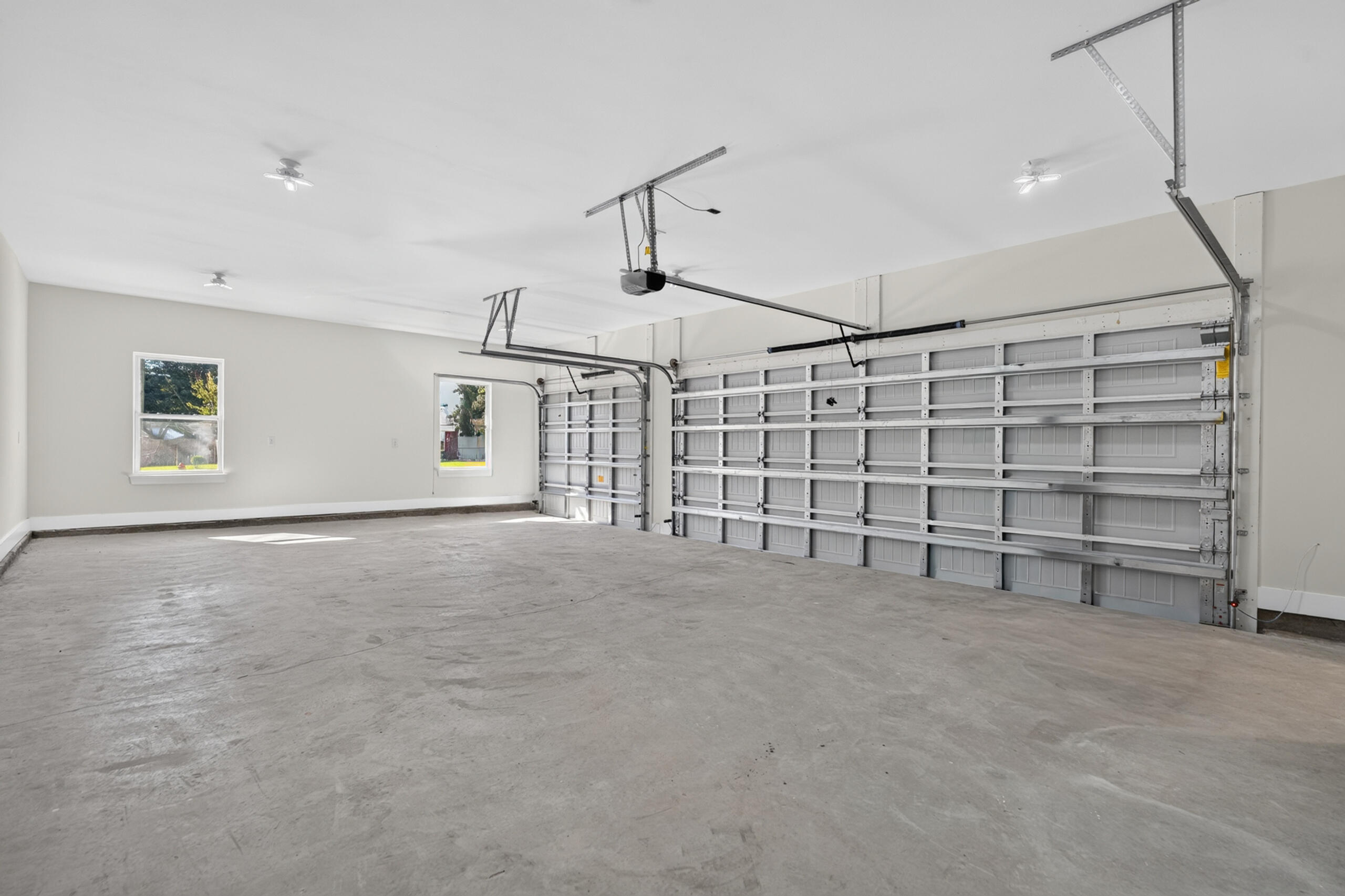 Vacant two-car garage with two large doors, a concrete floor, and side windows.