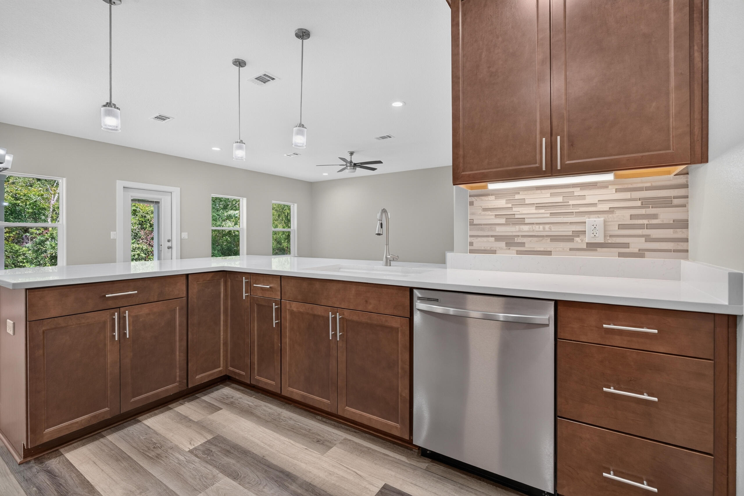 Kitchen with dark wood cabinets, white countertops, a long island, and stainless steel dishwasher.