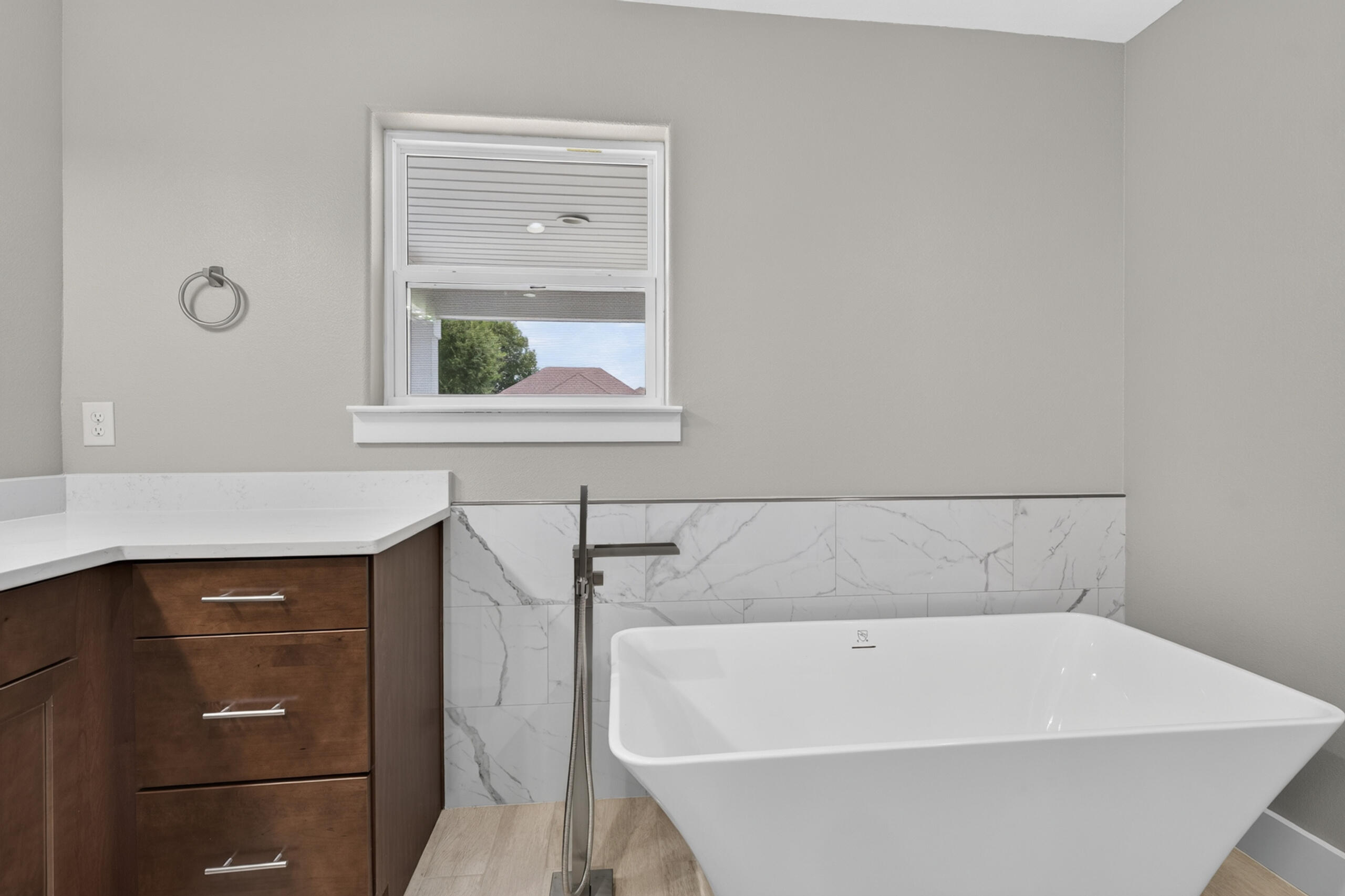 Bathroom with a freestanding soaking tub, marble-look tile, and dark wood vanity.