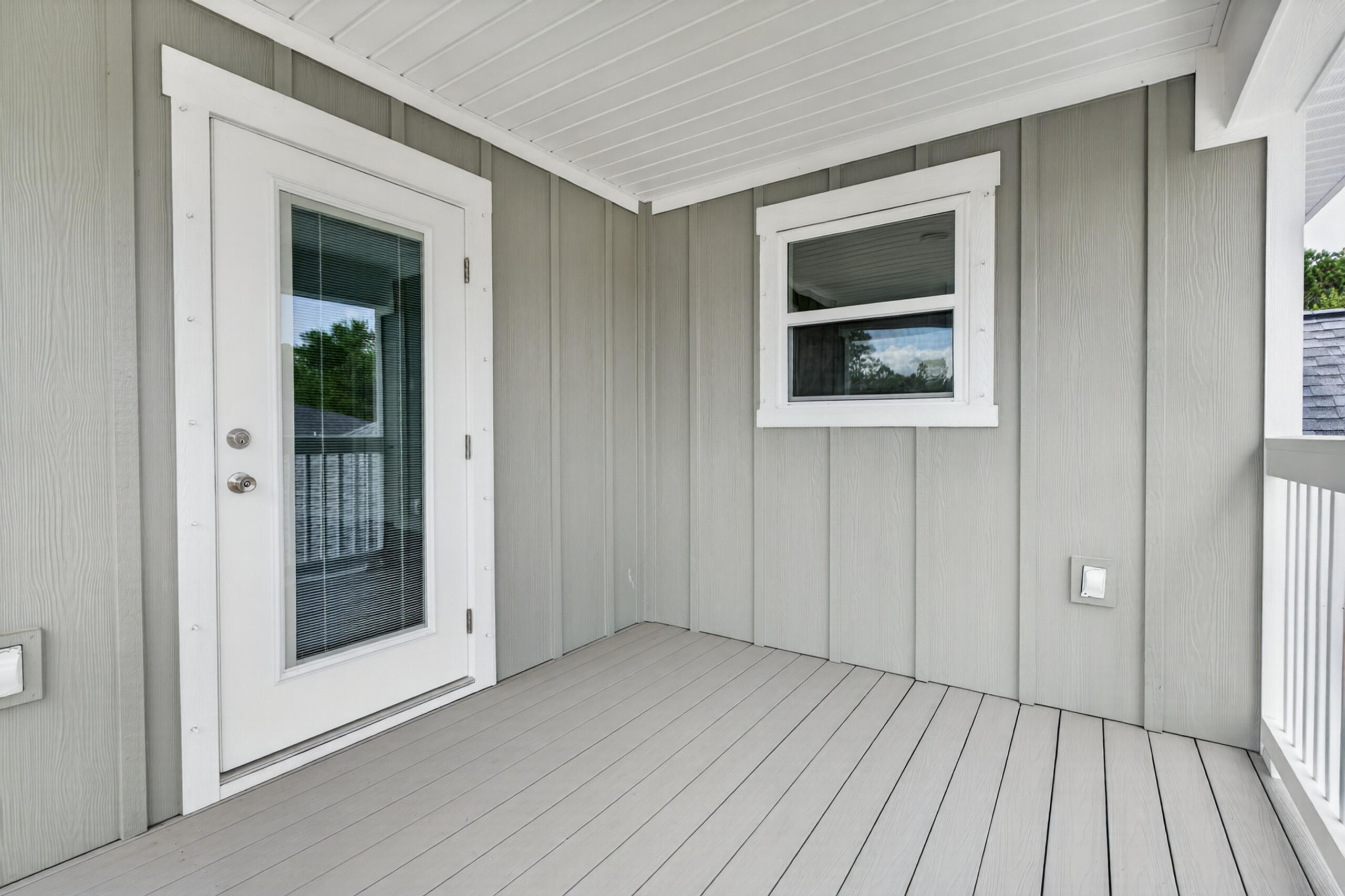 Covered porch with gray plank flooring, a white-framed glass door, and white railing.
