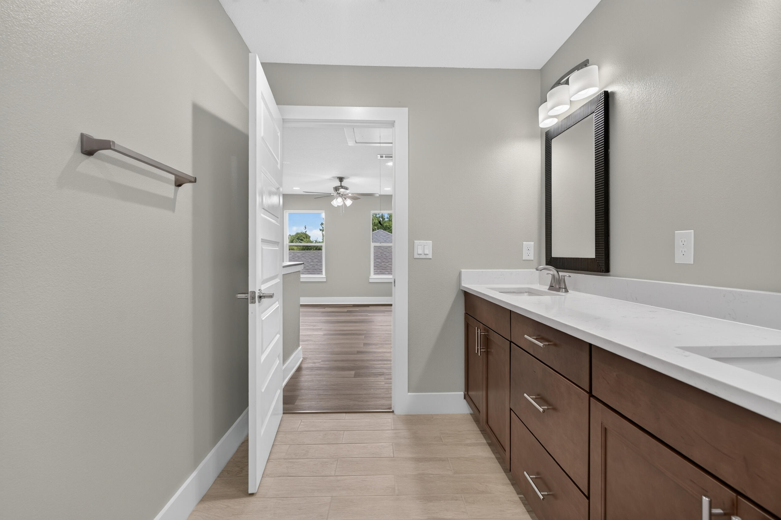 Bathroom with a long white vanity countertop, dark wood cabinets, and a large framed mirror.