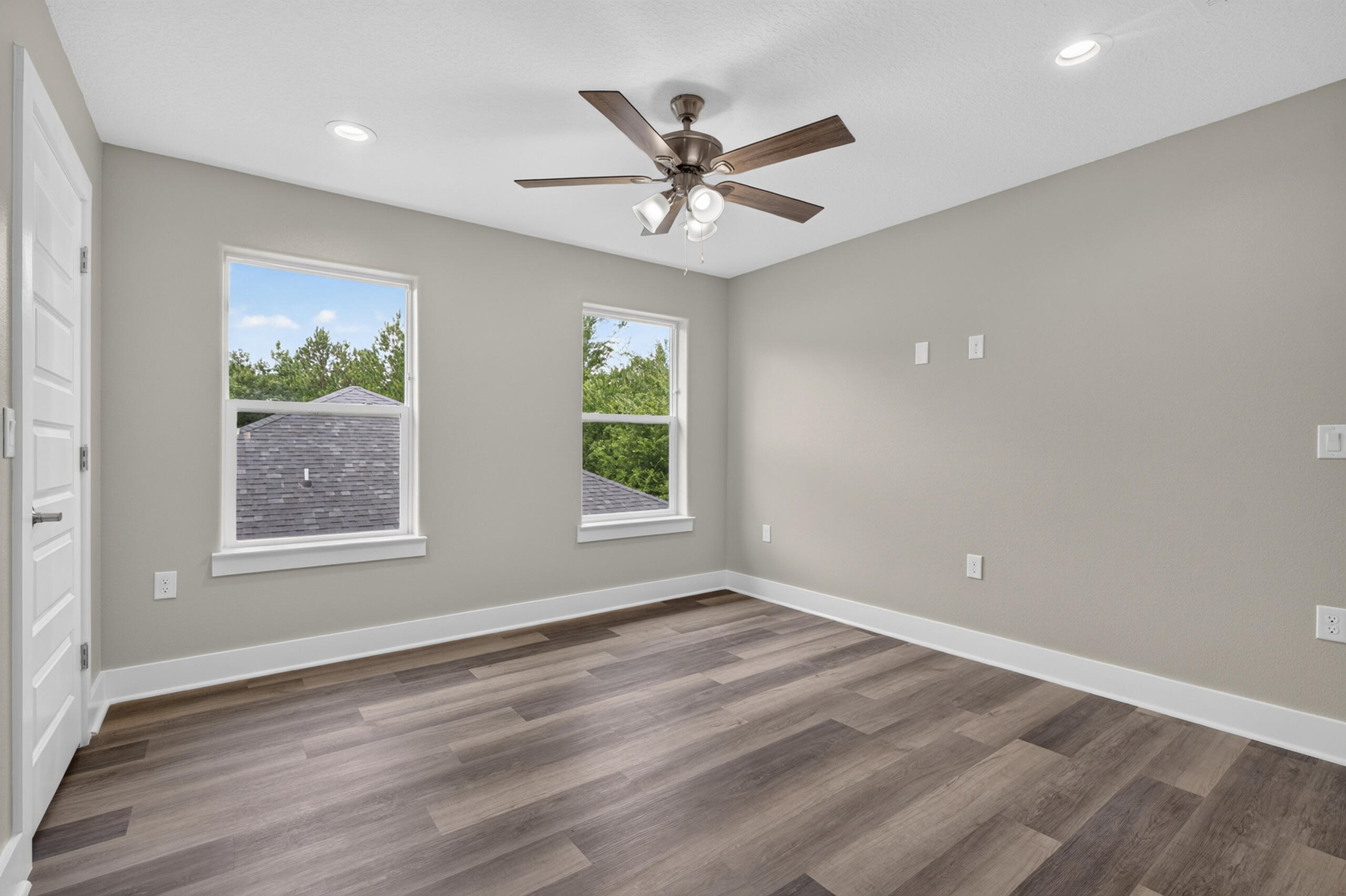 Empty room with two windows, a ceiling fan, and gray-brown plank flooring.