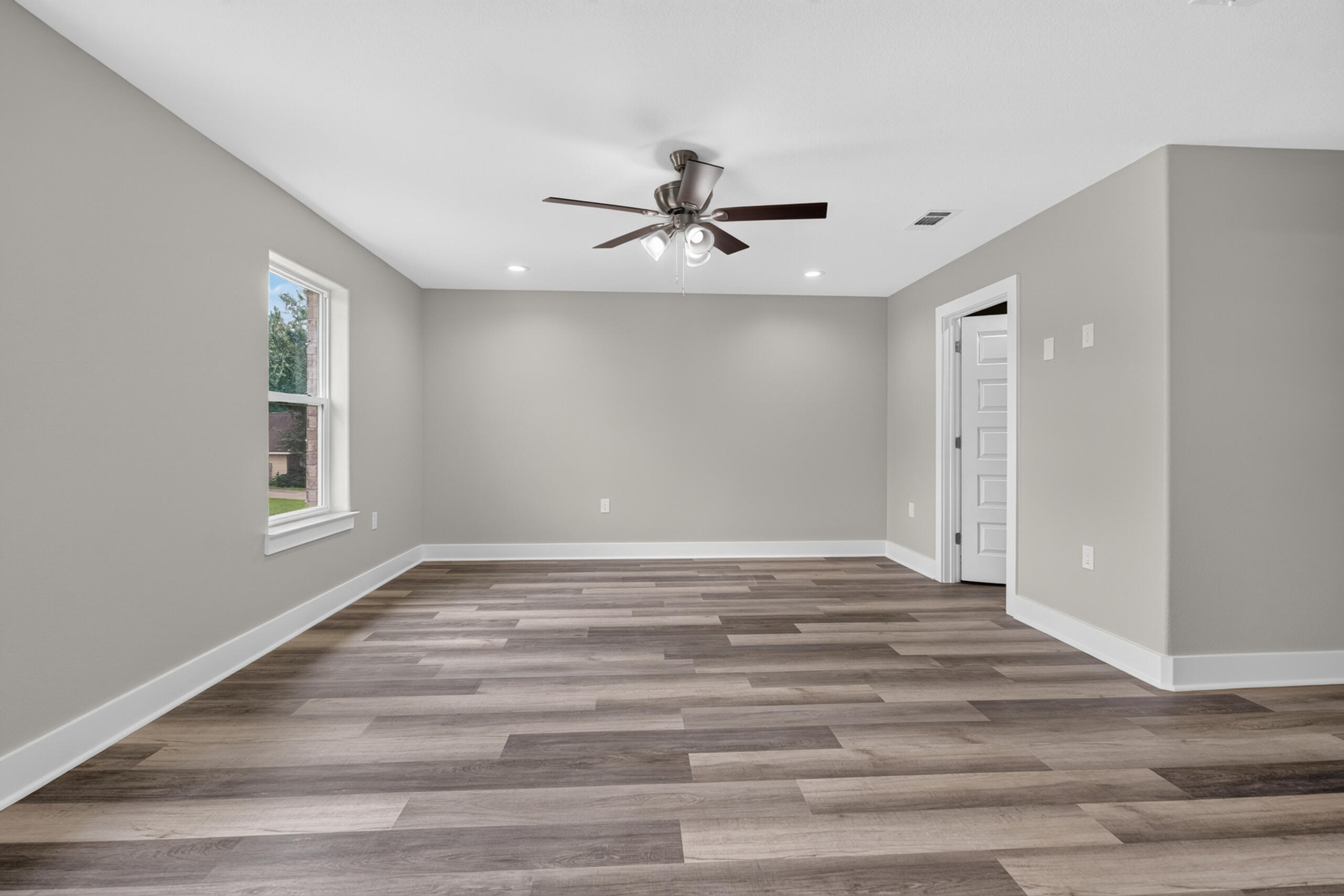 Empty room with wood-look plank flooring, a large window, and a ceiling fan.