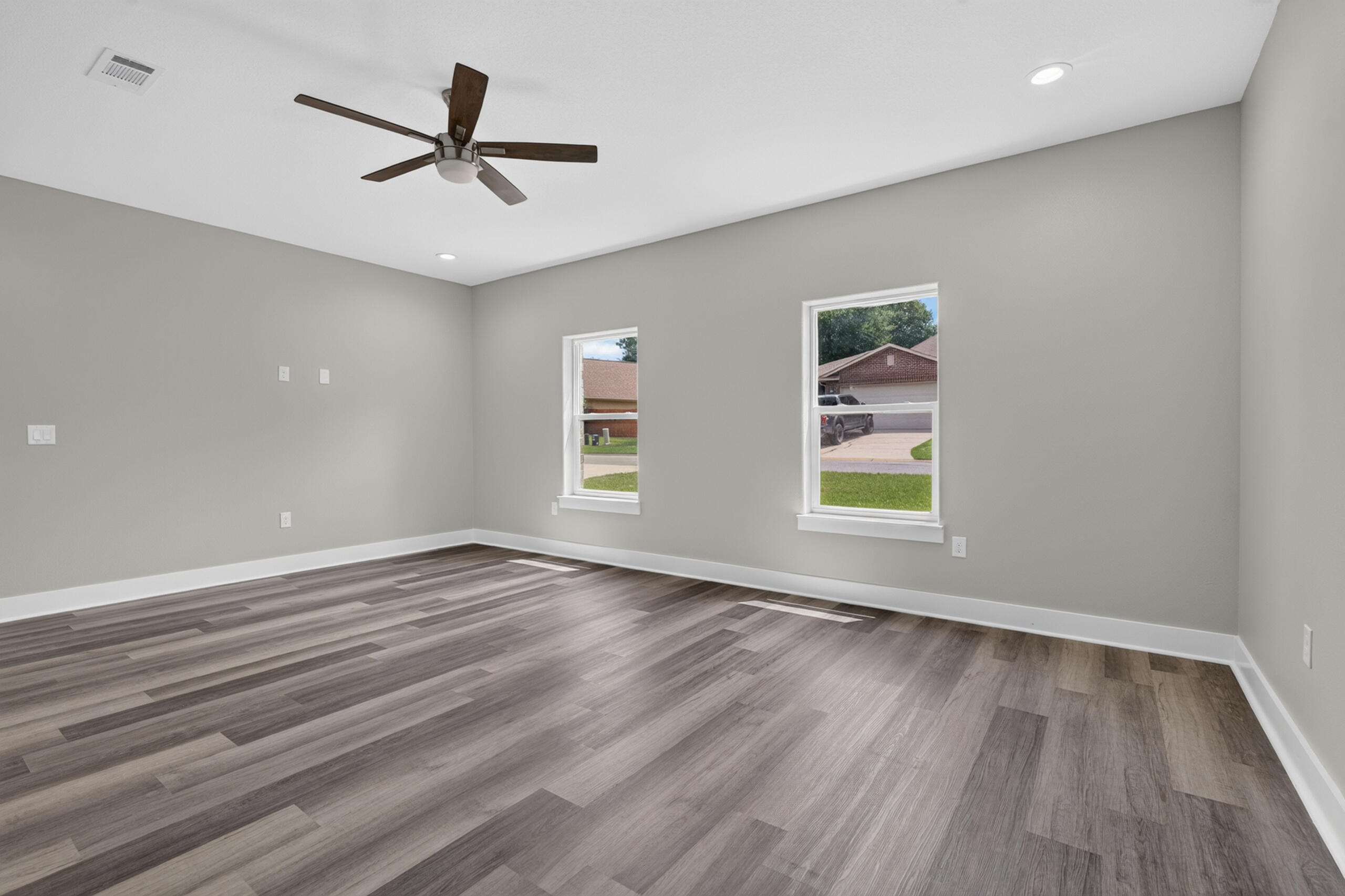 Empty room with gray walls, wood-look flooring, two windows, and a ceiling fan.