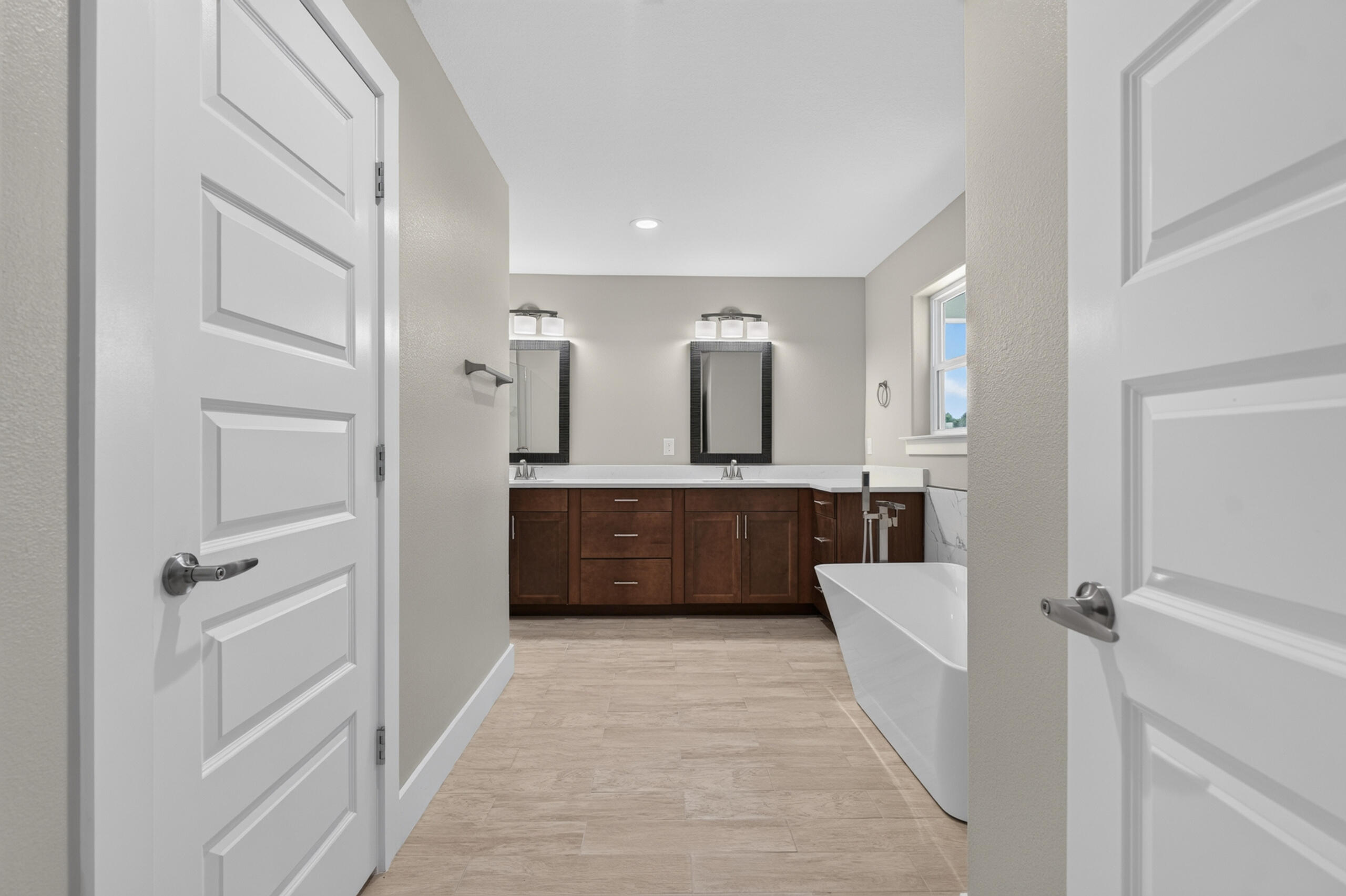 Bathroom with a dark double vanity, two mirrors, and a freestanding tub.