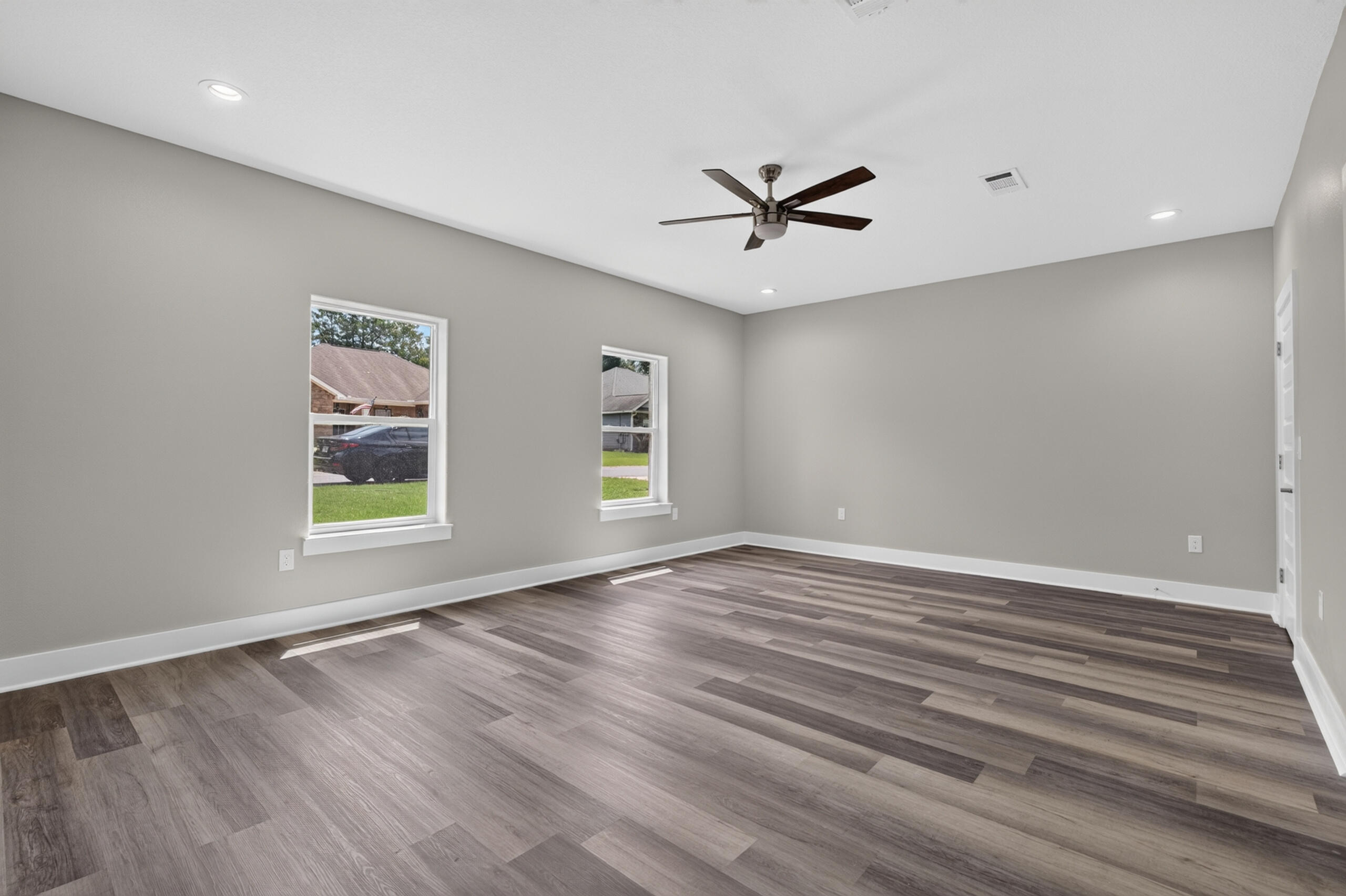 Empty room with gray walls, plank flooring, two windows, and a ceiling fan.