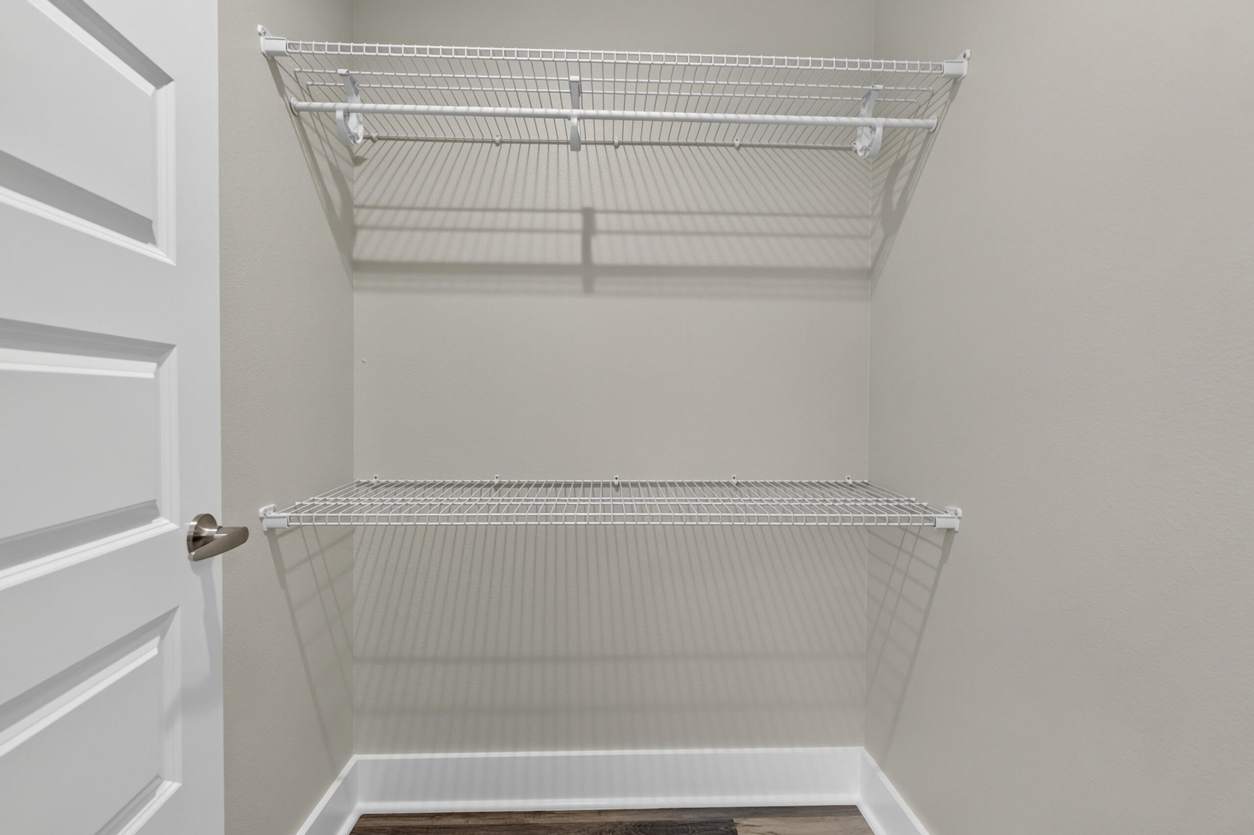 Walk-in closet with two white wire shelves and hanging rods above a wood-look floor.