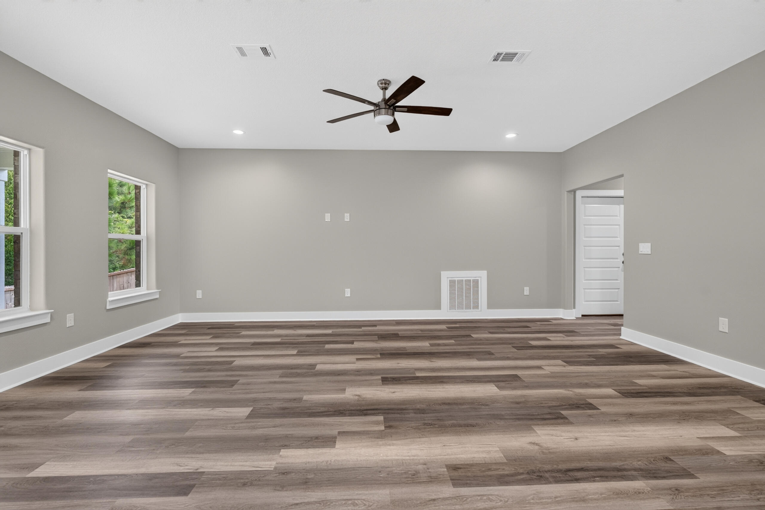 Empty living room with wood-look flooring, two windows, and a dark-bladed ceiling fan.