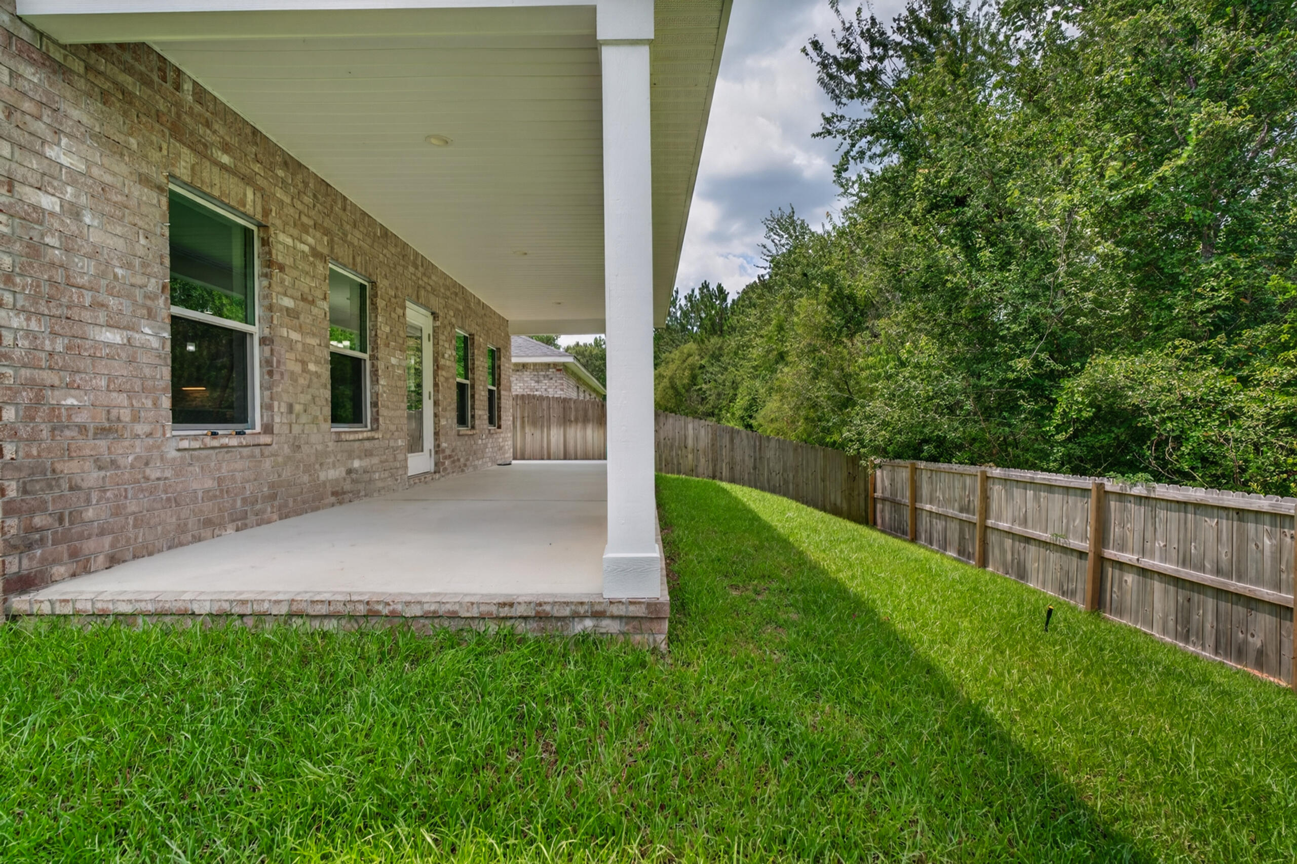 Covered patio along a brick house beside a fenced grassy yard.
