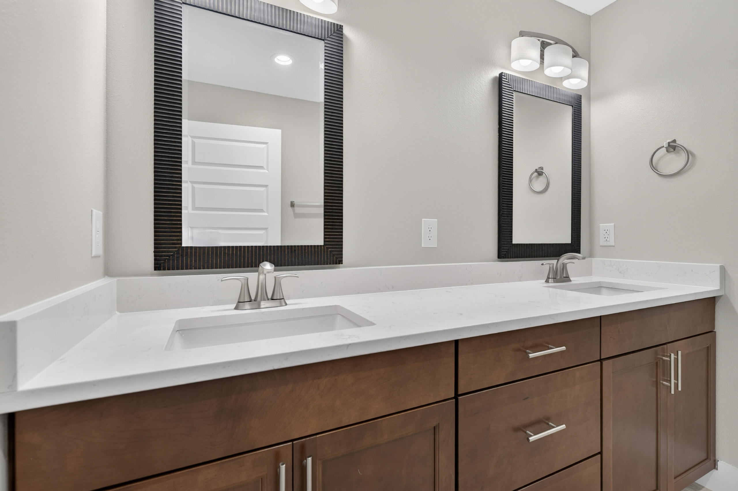 Bathroom vanity with two sinks, a white countertop, dark wood cabinets, and framed mirrors.
