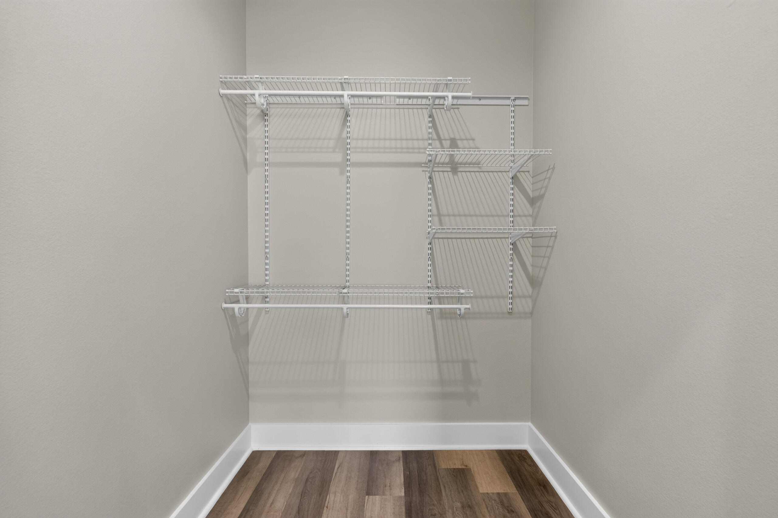 Empty walk-in closet with white wire shelving and wood-look plank flooring.