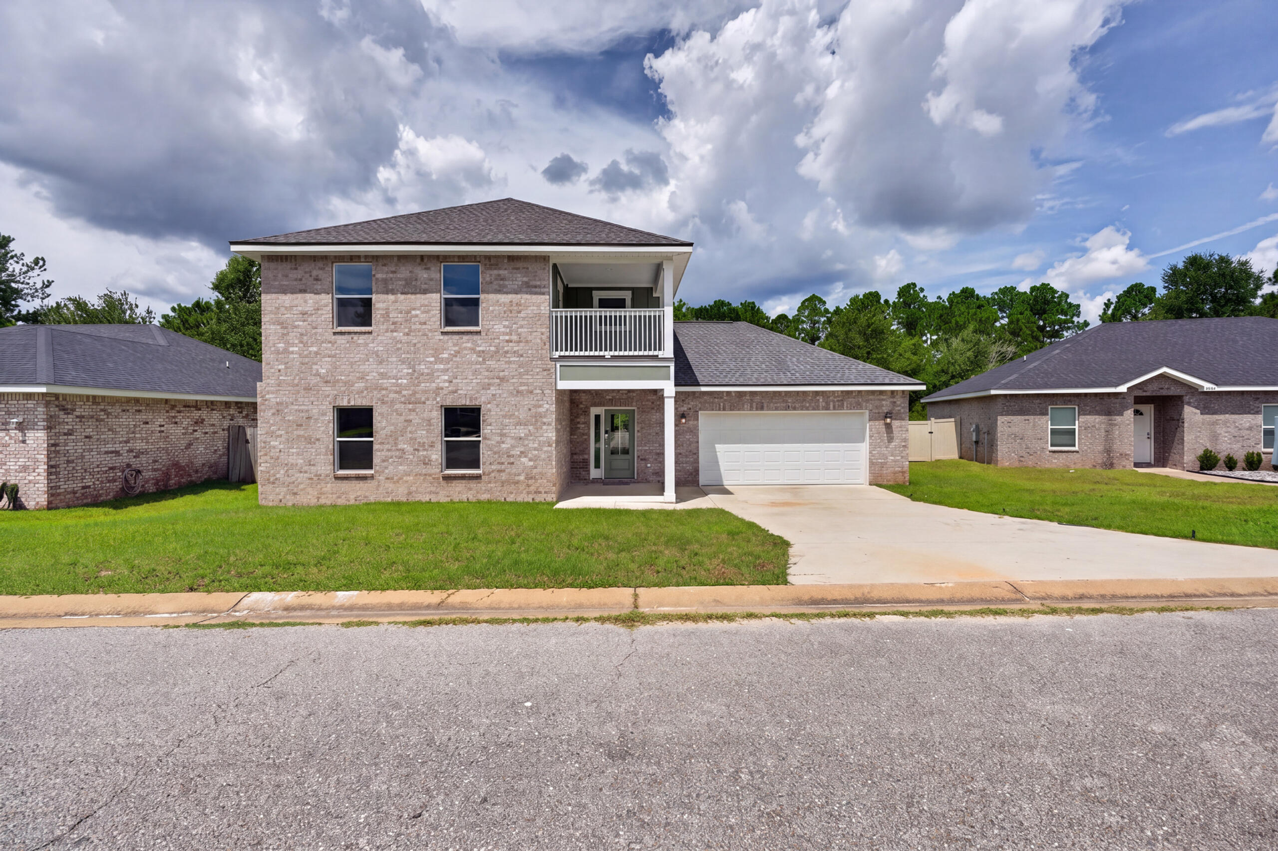 Two-story brick house with a covered balcony, attached garage, driveway, and front lawn.