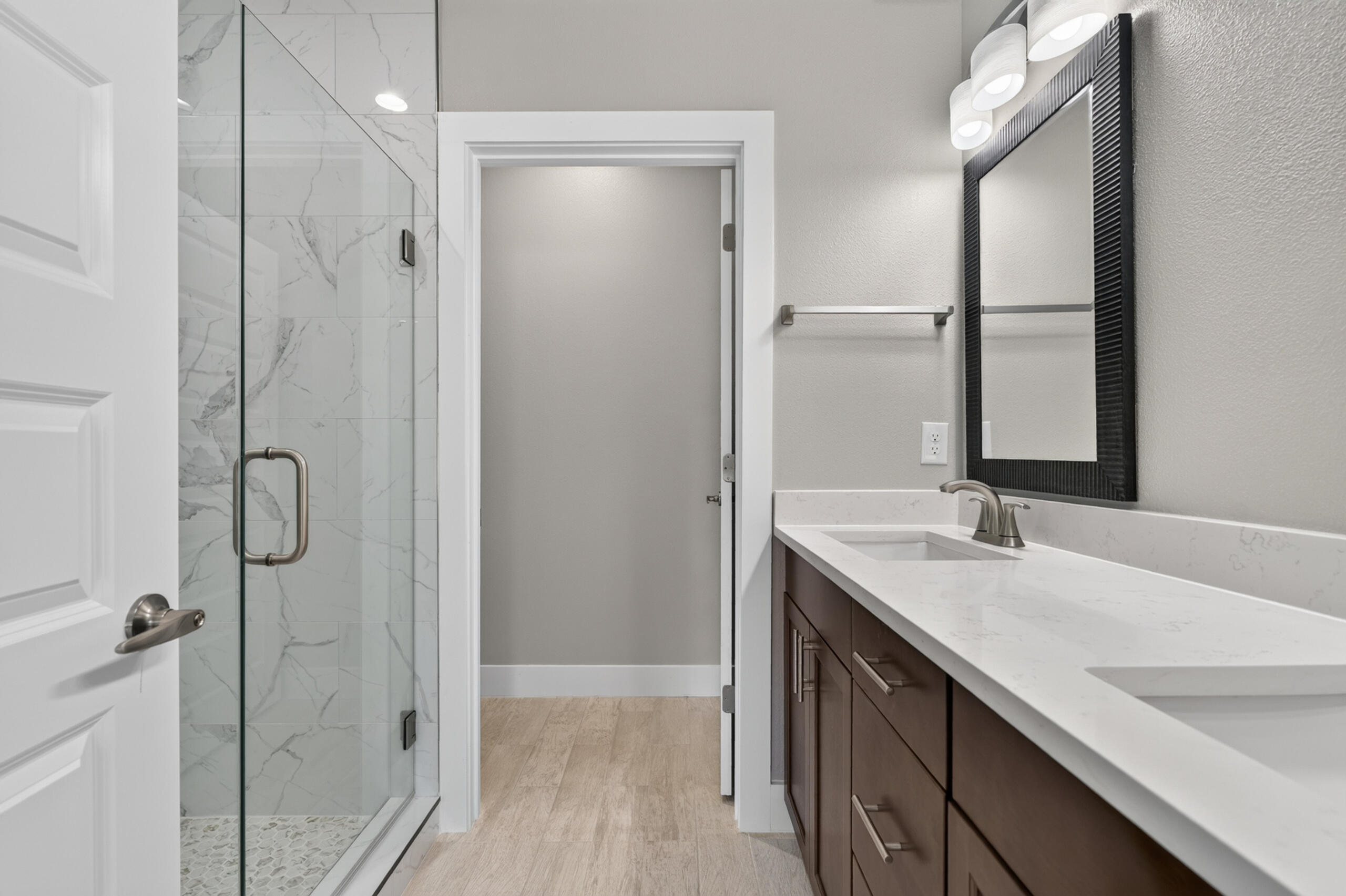 Bathroom with a marble-look glass shower and dark wood vanity beneath a large black-framed mirror.