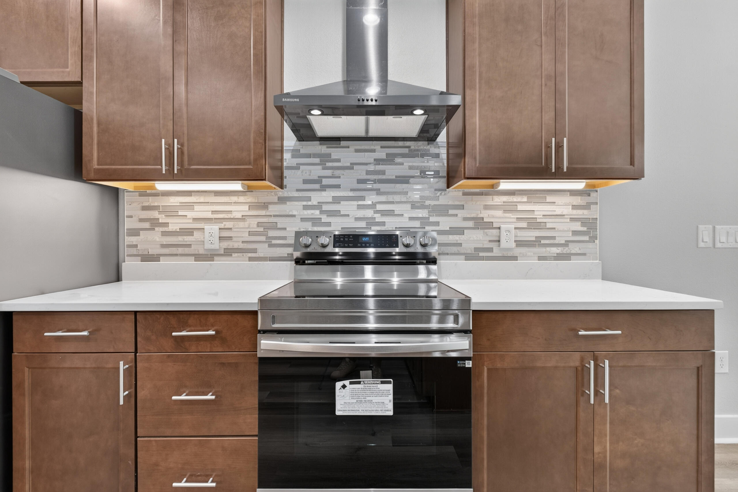 Kitchen with brown cabinets, a stainless steel range and hood, and a gray tile backsplash.