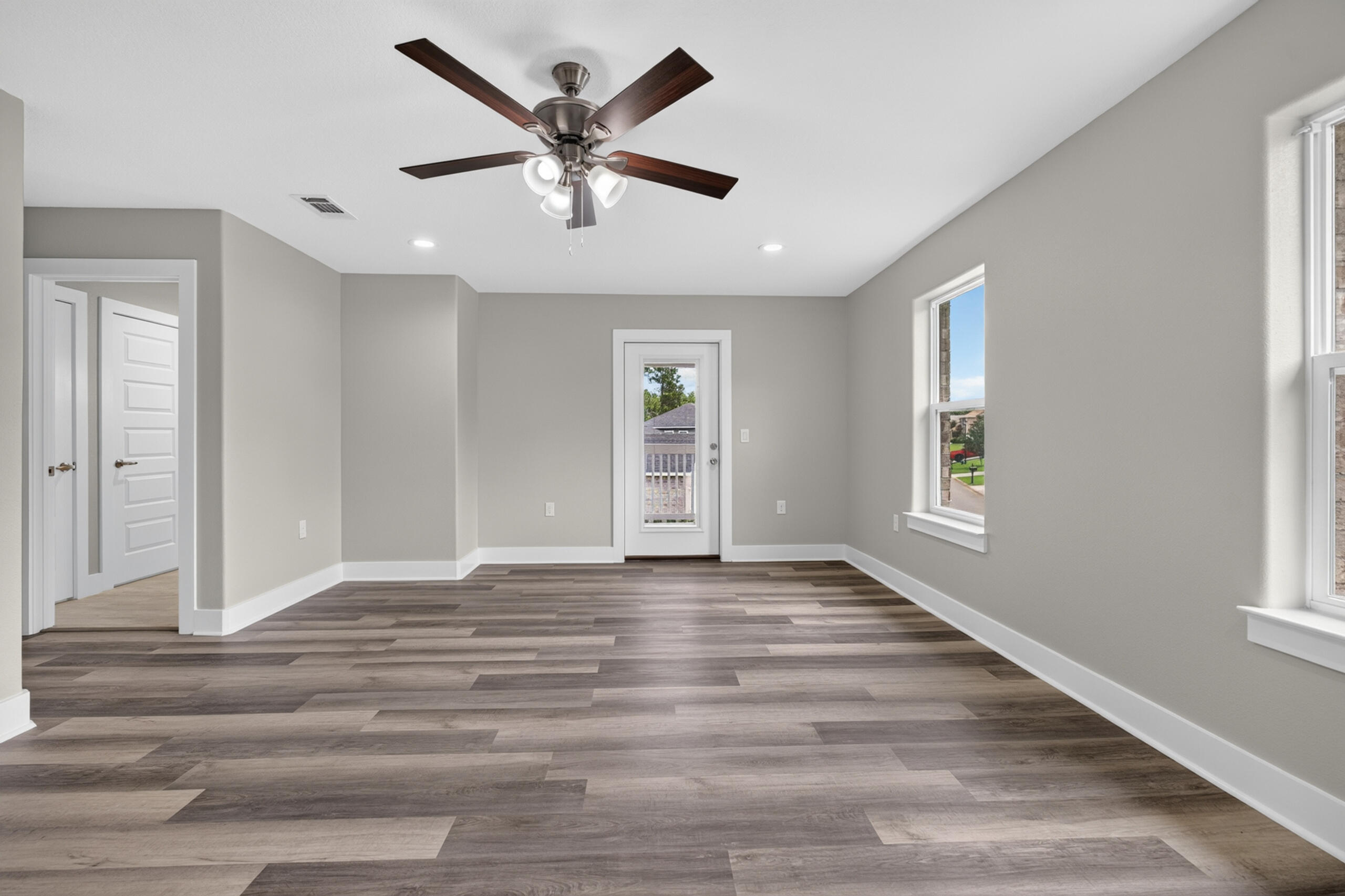 Empty living room with wide-plank flooring, a ceiling fan, and several windows.