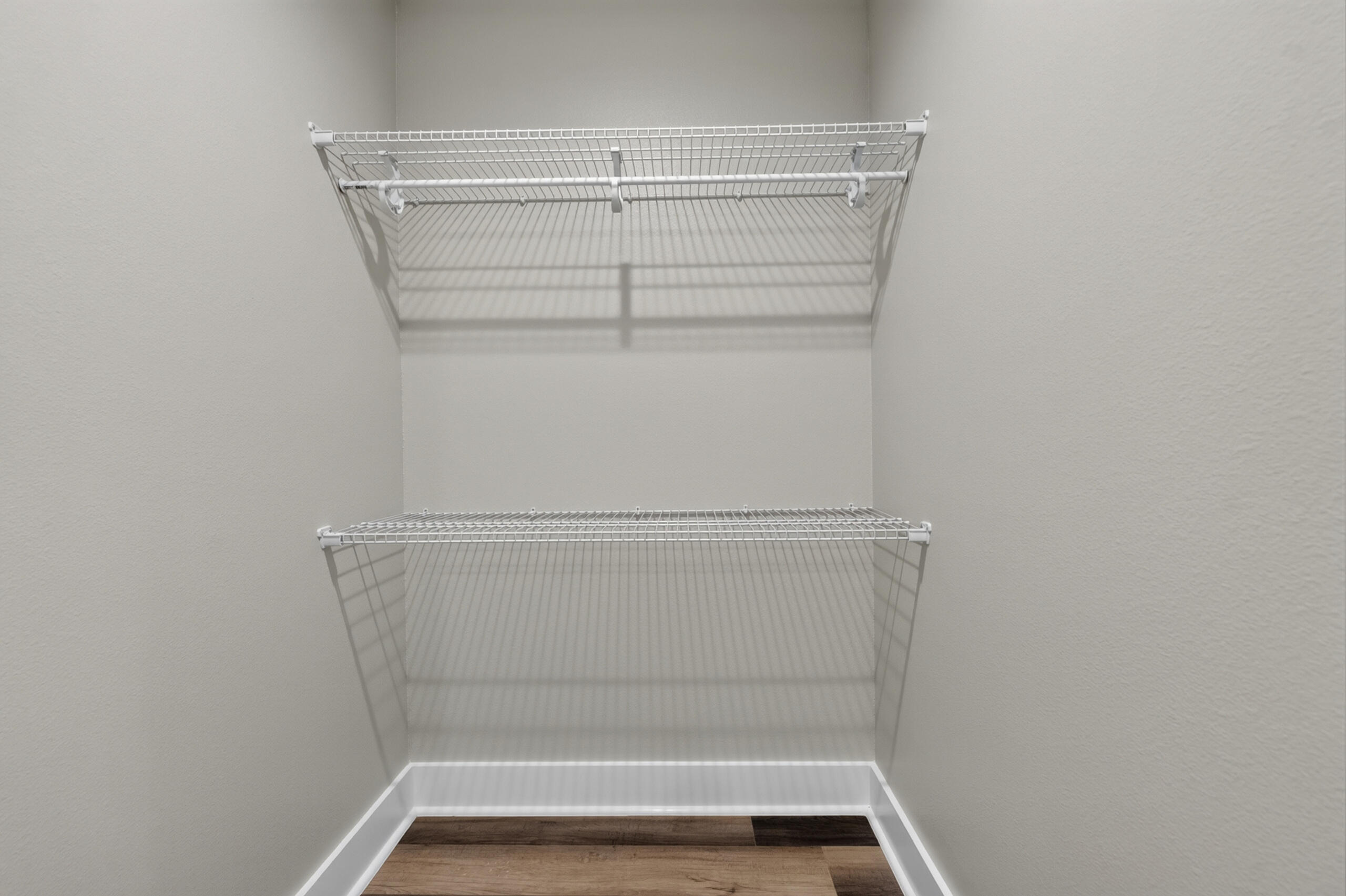 Empty walk-in closet with two tiers of white wire shelving and wood-look flooring.
