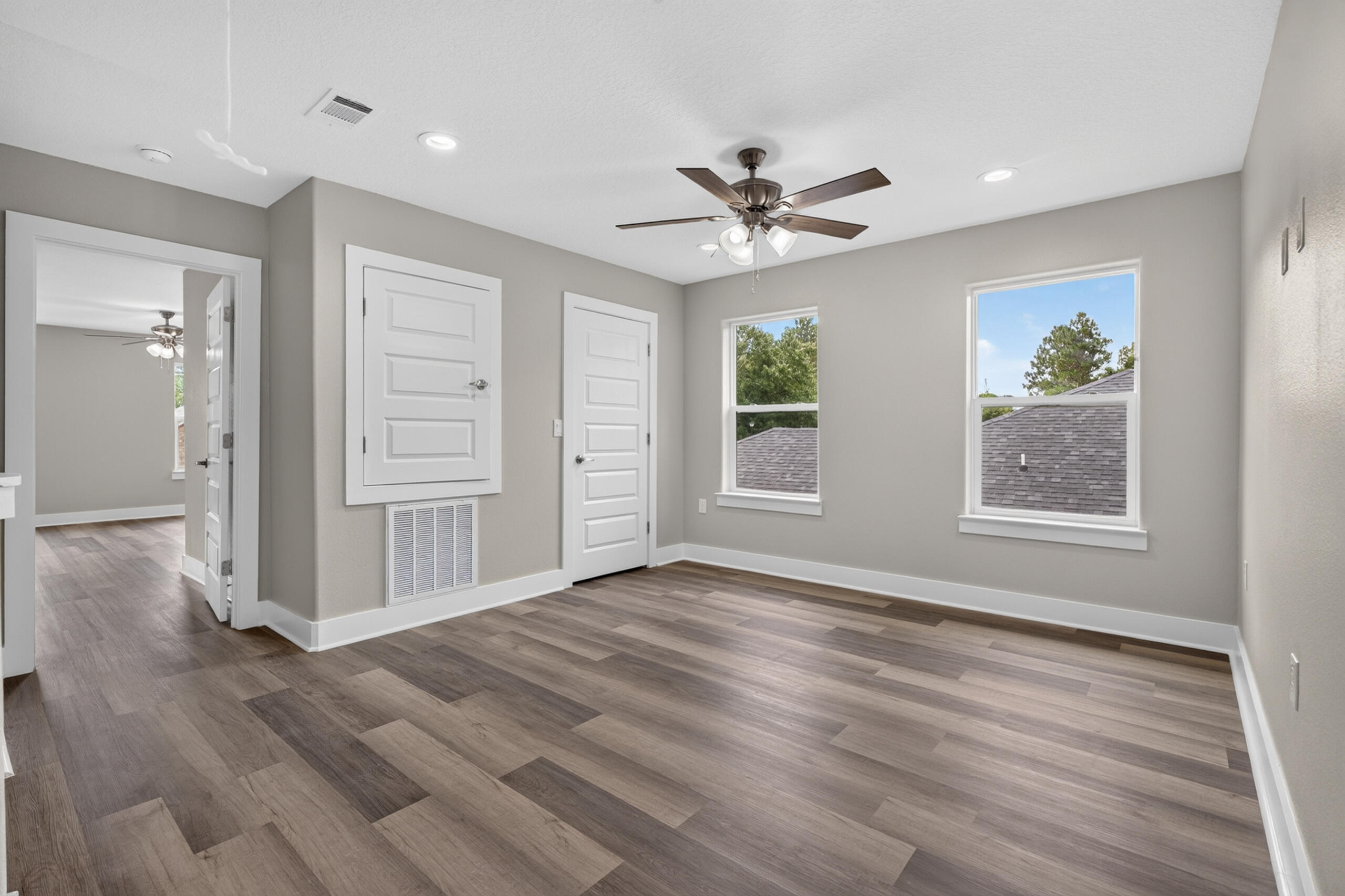 Vacant bedroom with plank flooring, two windows, and a ceiling fan.