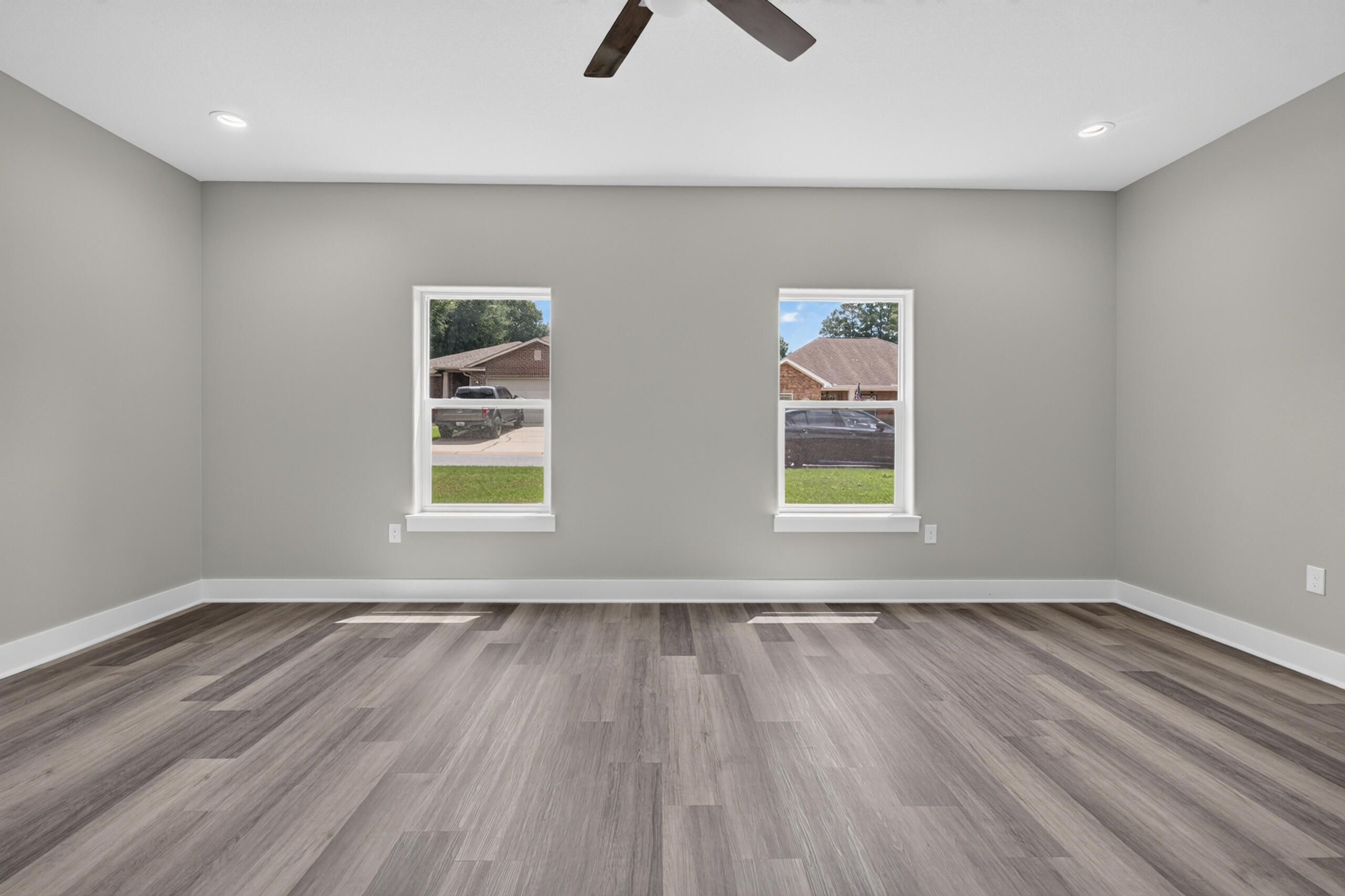 Empty room with gray wood-look flooring, two windows, and a ceiling fan.