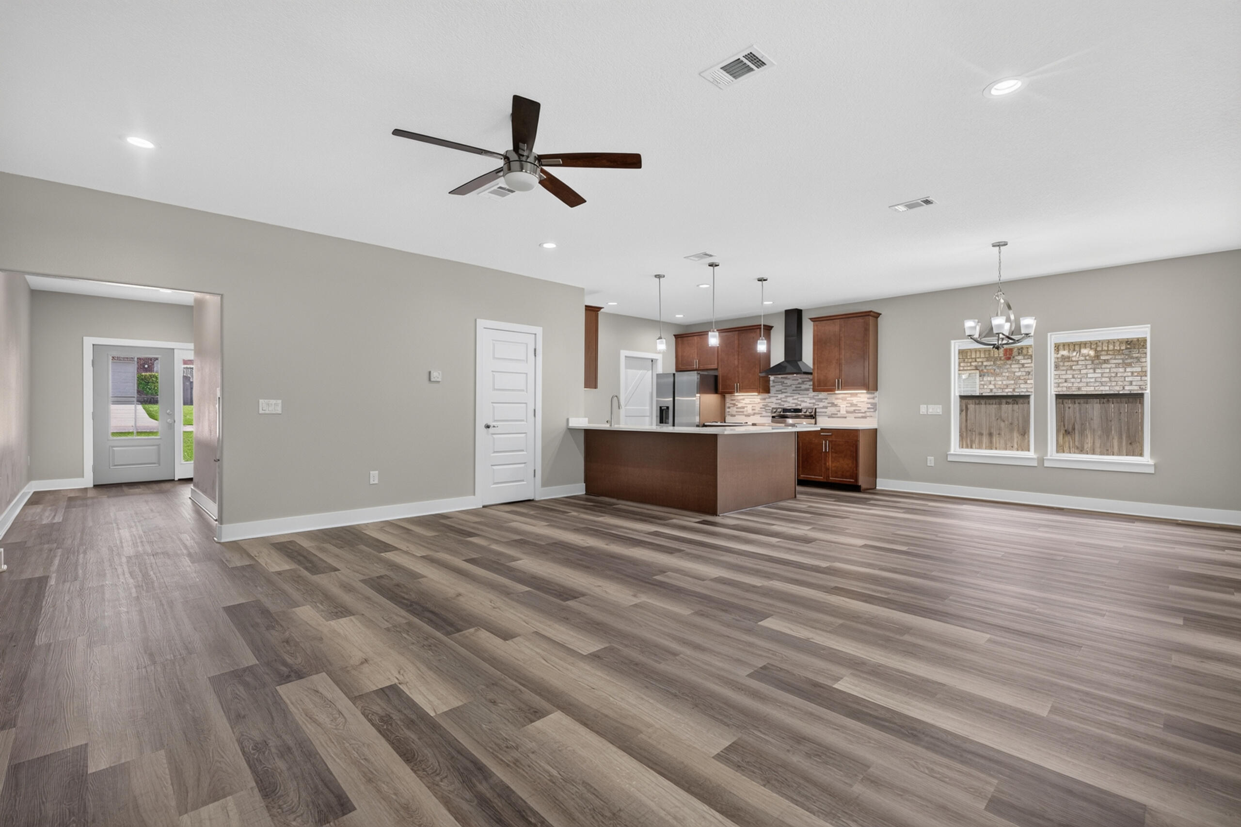 Open-plan living area and kitchen with a large island, dark wood cabinets, and multitone plank flooring.