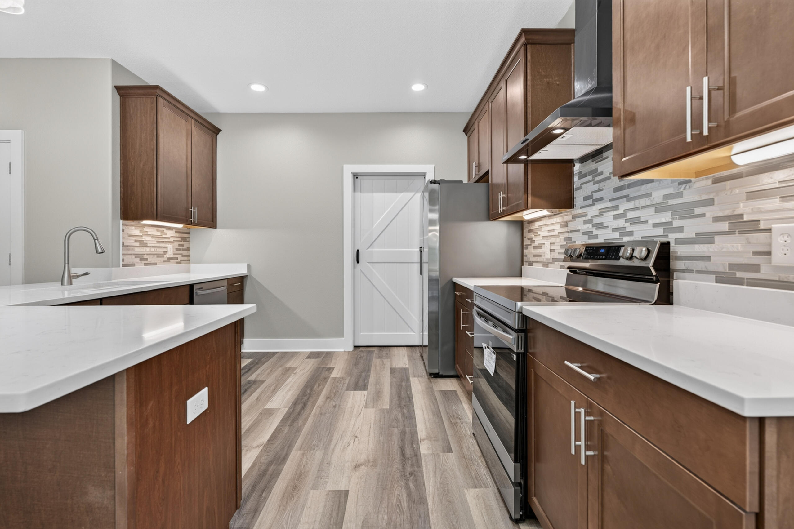 Kitchen with dark wood cabinets, white countertops, stainless steel appliances, and a gray tile backsplash.