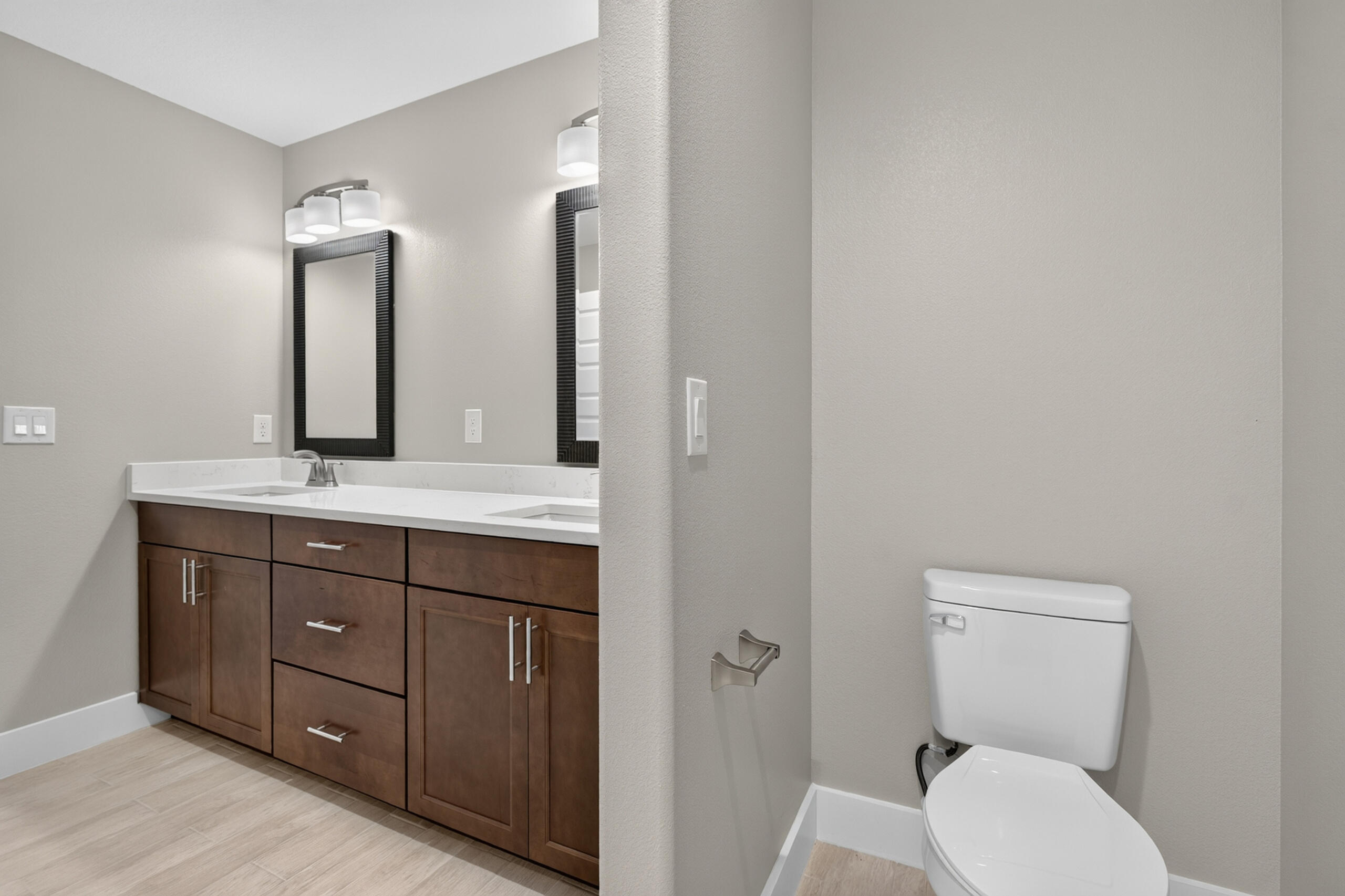 Bathroom with a dark wood double-sink vanity and a toilet behind a partial wall.