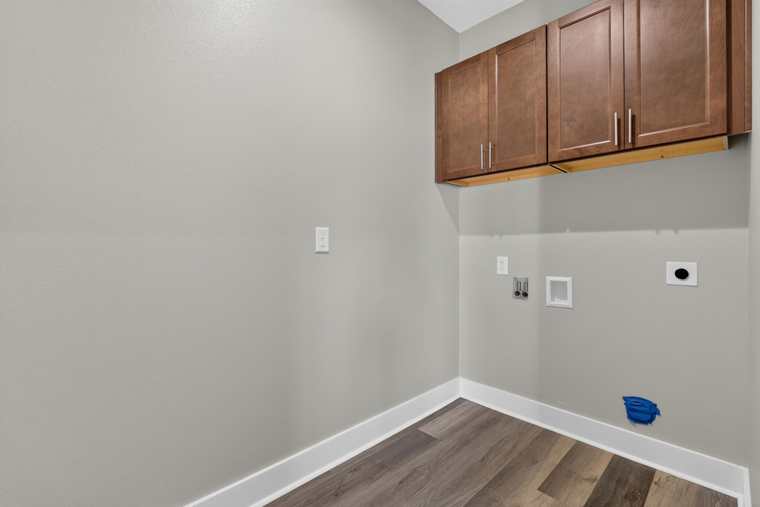 Laundry room with upper cabinets, exposed appliance connections, and wood-look flooring.