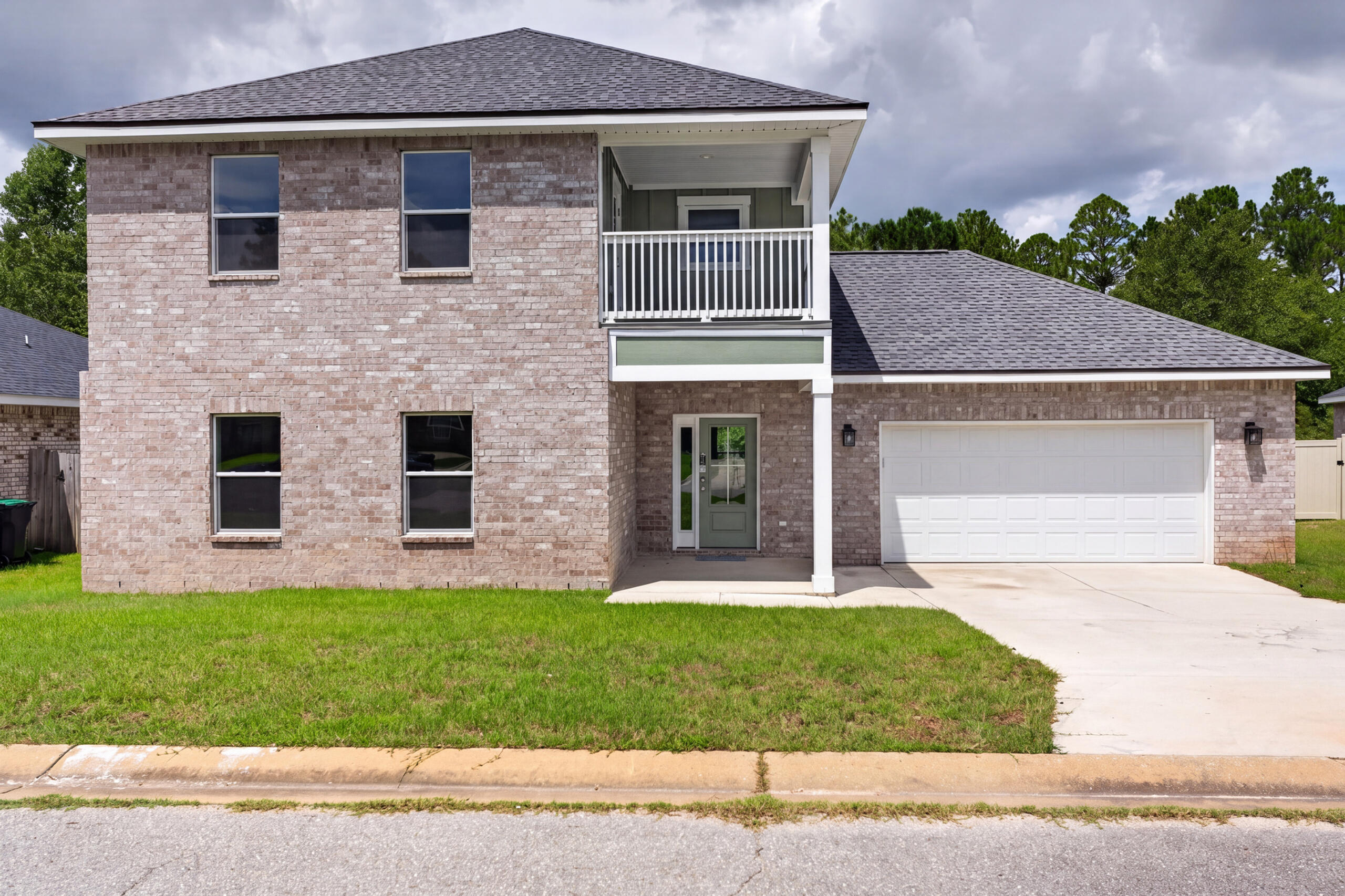 Two-story brick home with an upper balcony, attached garage, and front lawn.