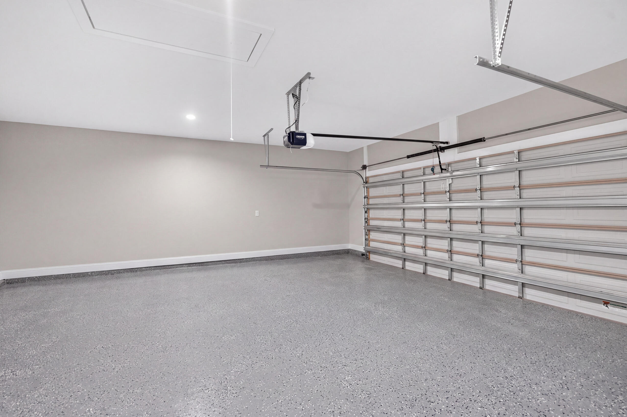 Empty garage with a speckled epoxy floor and overhead garage door opener.