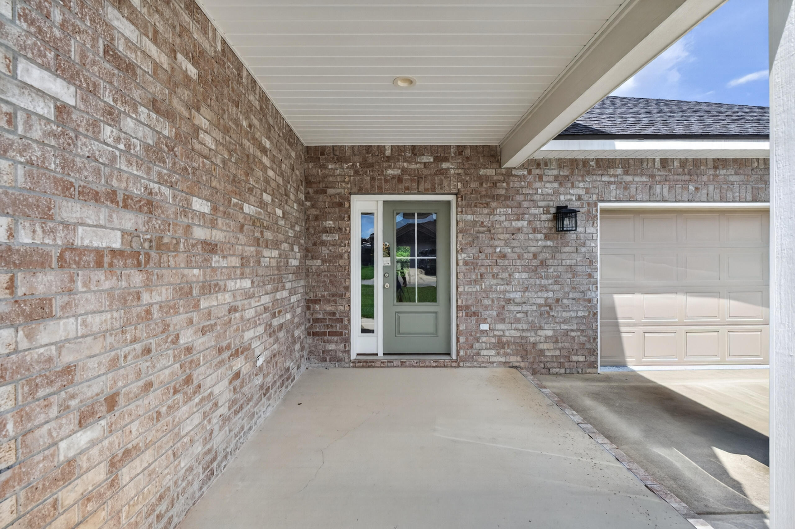 Brick home’s covered front porch with a pale green glass-paneled door beside the garage.
