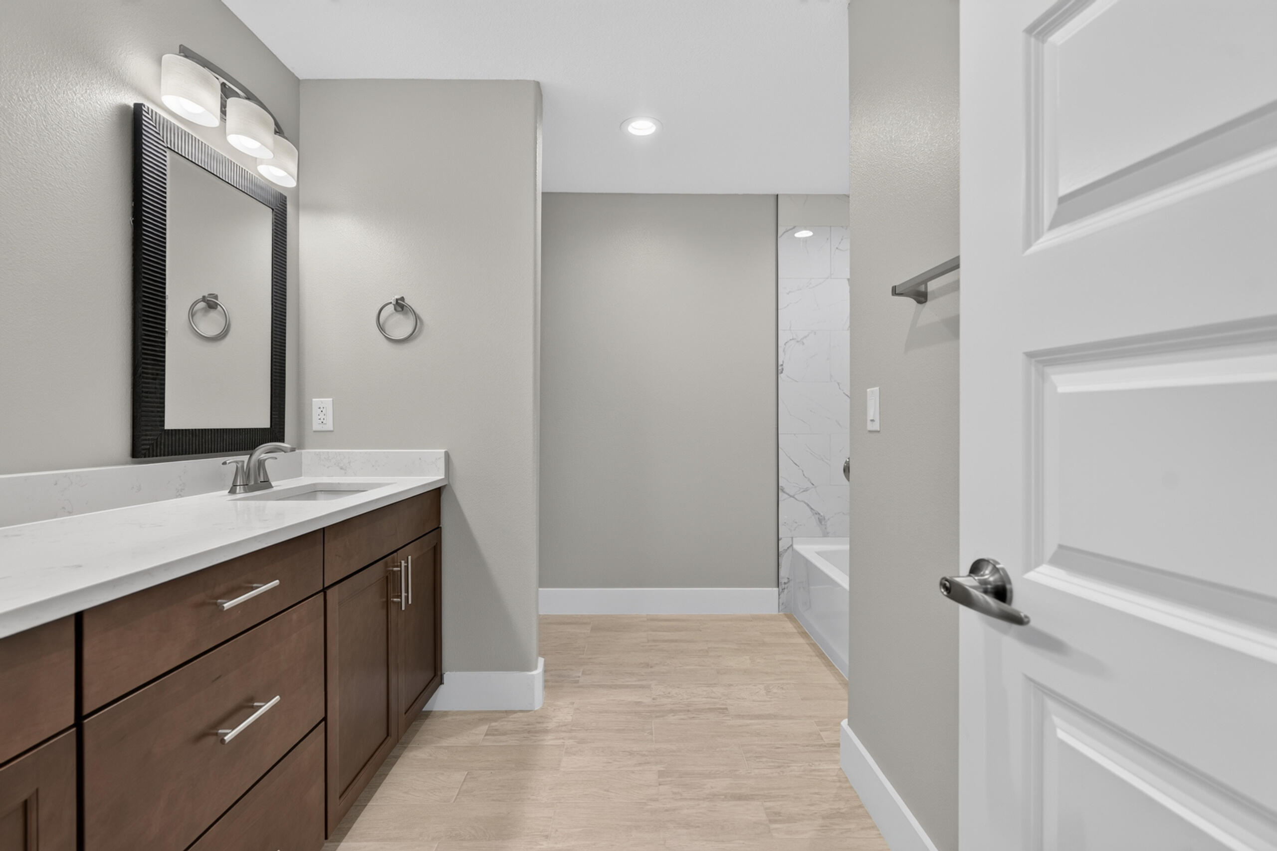 Bathroom with dark wood vanity, white countertop, black-framed mirror, and marble-look tub surround.