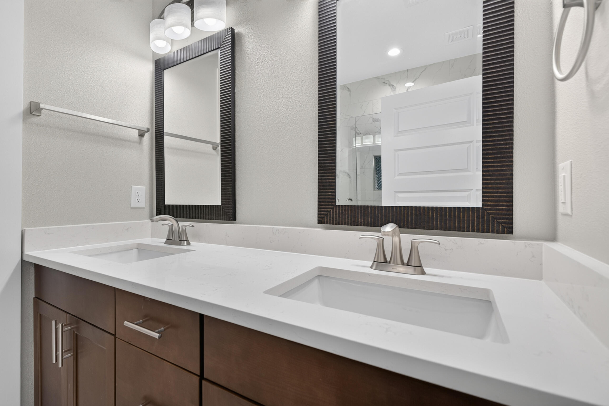 Bathroom vanity with two sinks, a white veined counter, dark wood cabinets, and large framed mirrors.