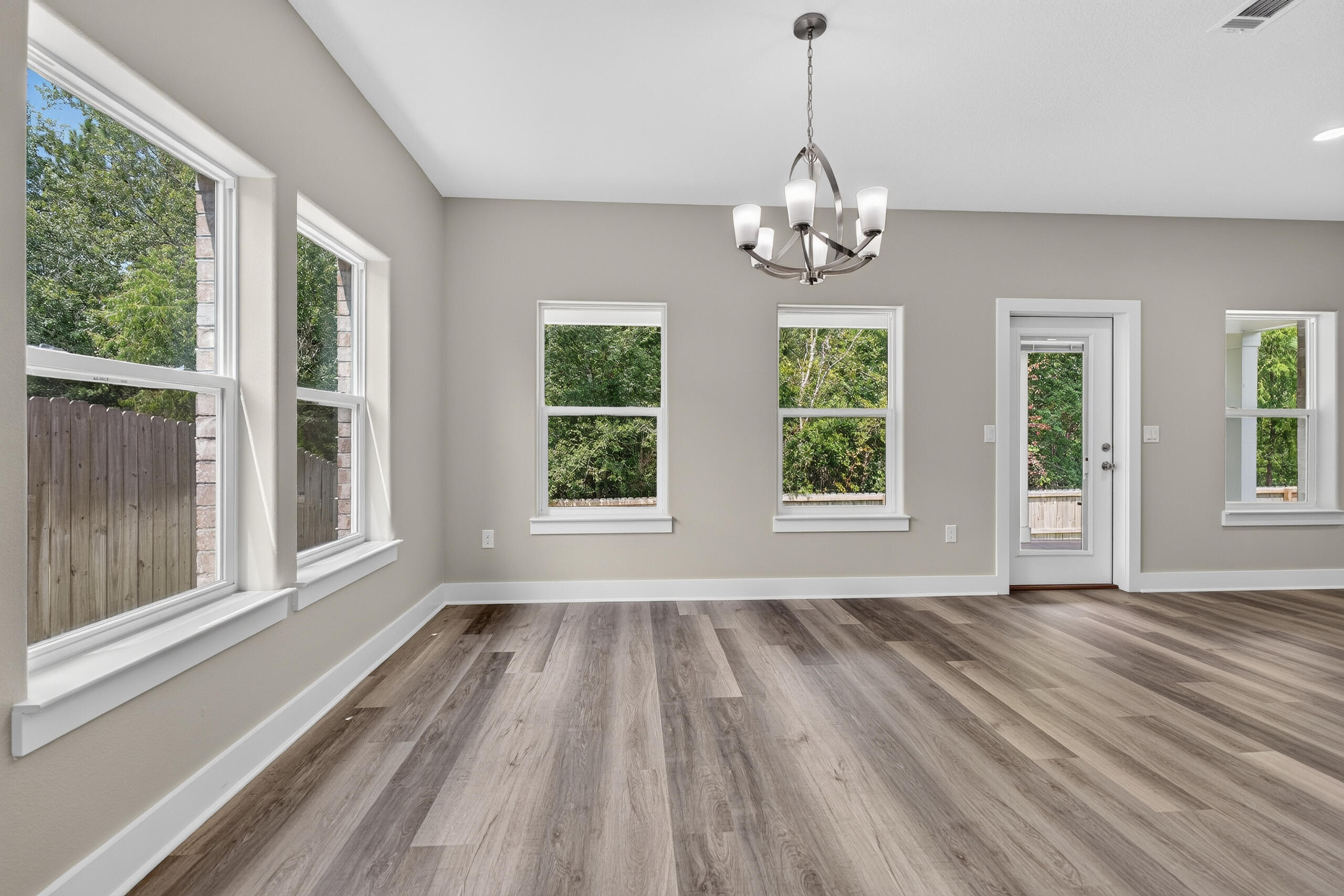 Empty room with wood-look flooring, large windows, and a chandelier