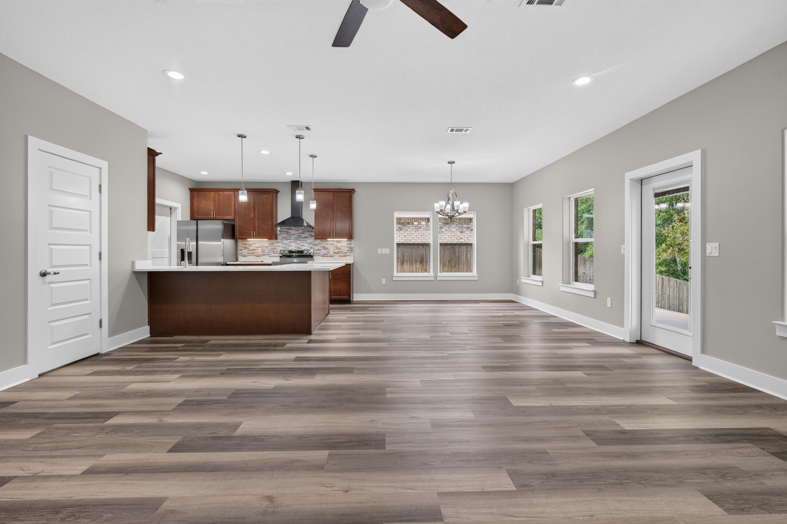 Open-plan kitchen and dining area with a large island, dark wood cabinets, and gray wood-look flooring.