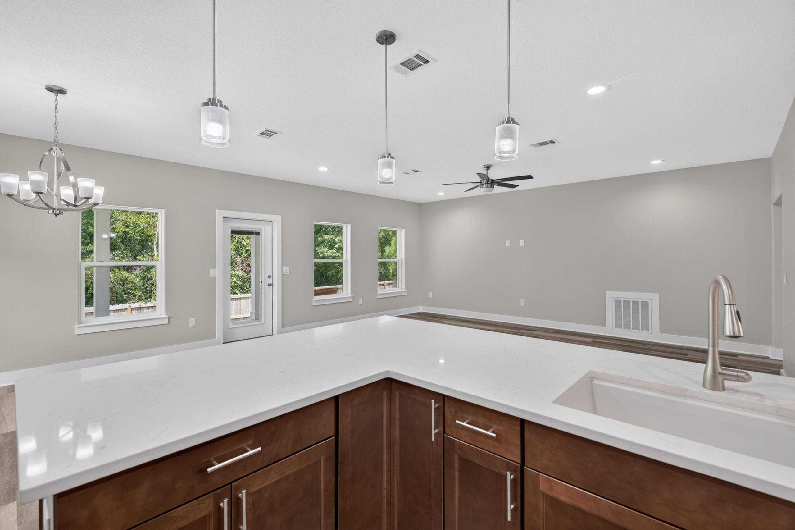 Open kitchen with a white quartz island, dark wood cabinets, and windows overlooking greenery.