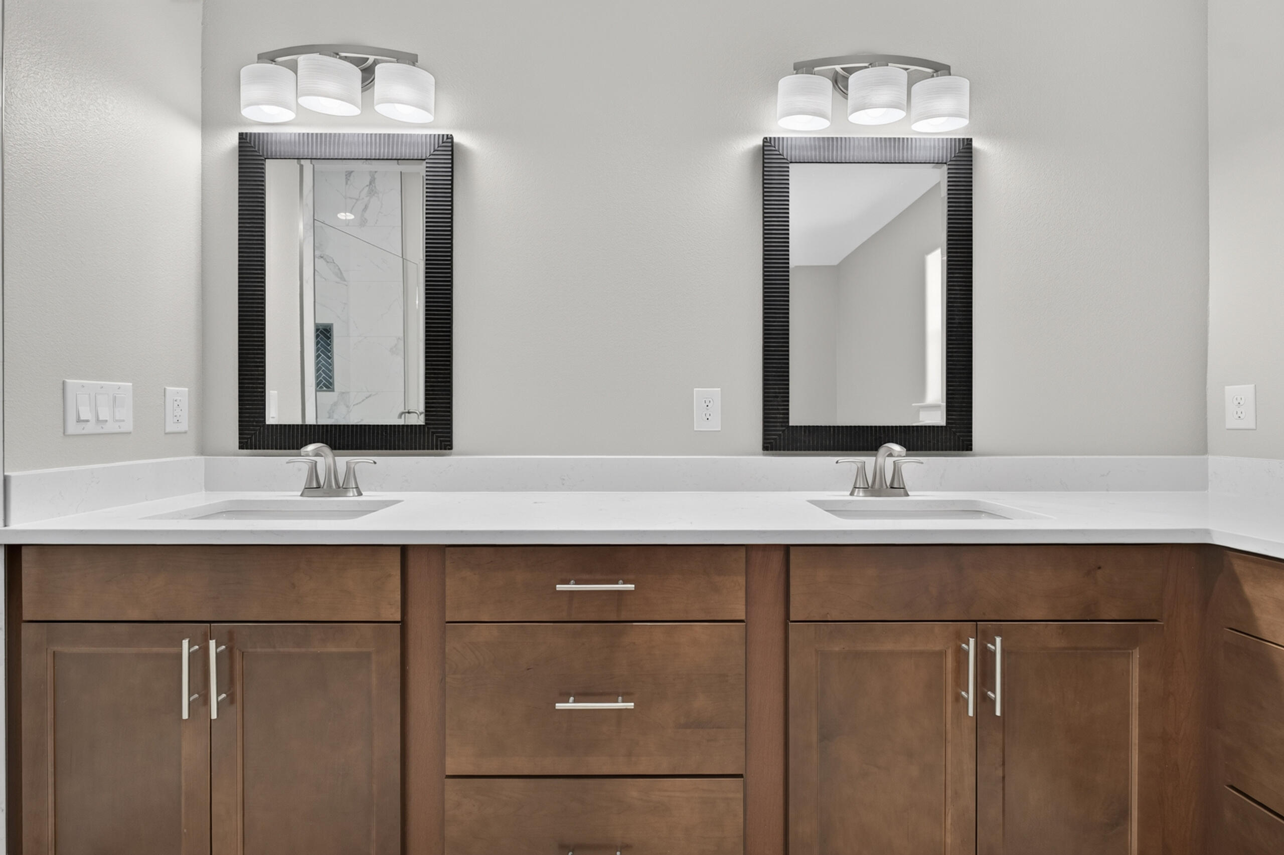Bathroom vanity with double sinks, white countertop, brown cabinetry, and black-framed mirrors.