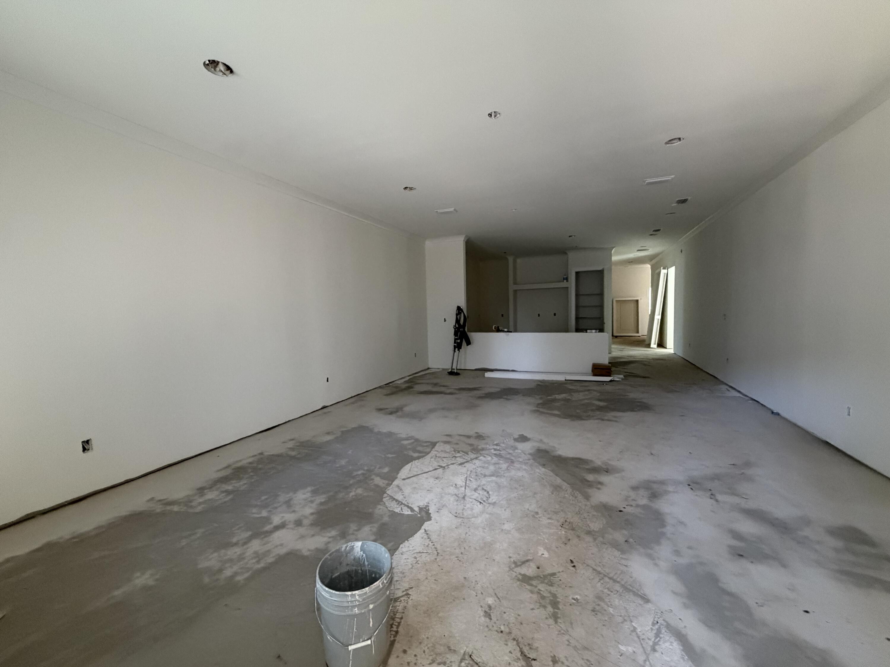 Unfinished open-plan interior with a bare concrete floor and partial kitchen counter at the back.