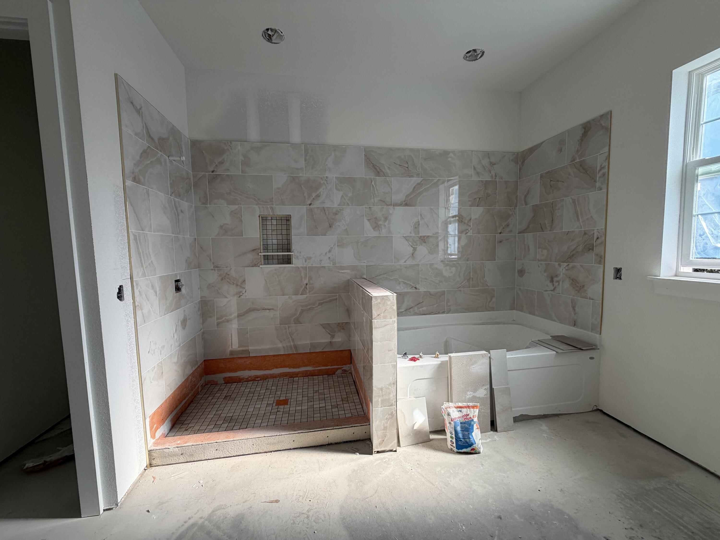 Unfinished bathroom with a marble-look tiled shower and a white soaking tub.