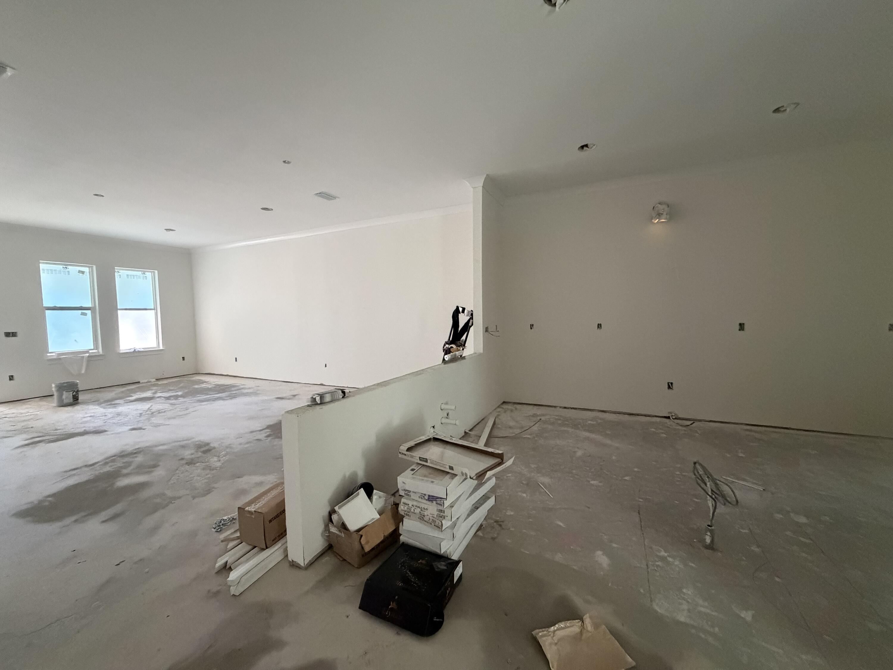 Unfinished open-plan interior with concrete floors, two windows, and construction materials beside a half-height partition.