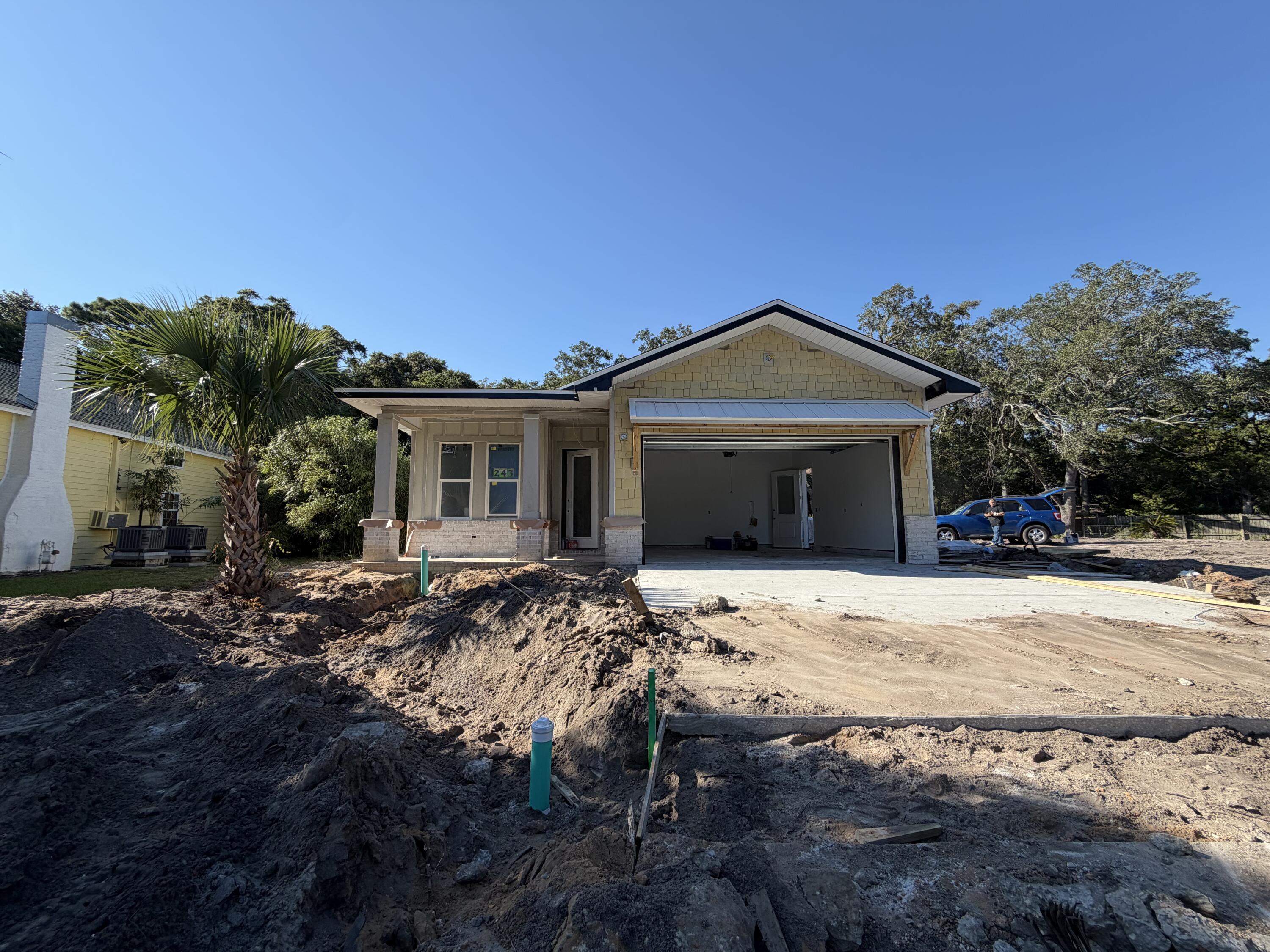 Single-story home under construction with an open garage, yellow siding, and an unfinished dirt driveway.
