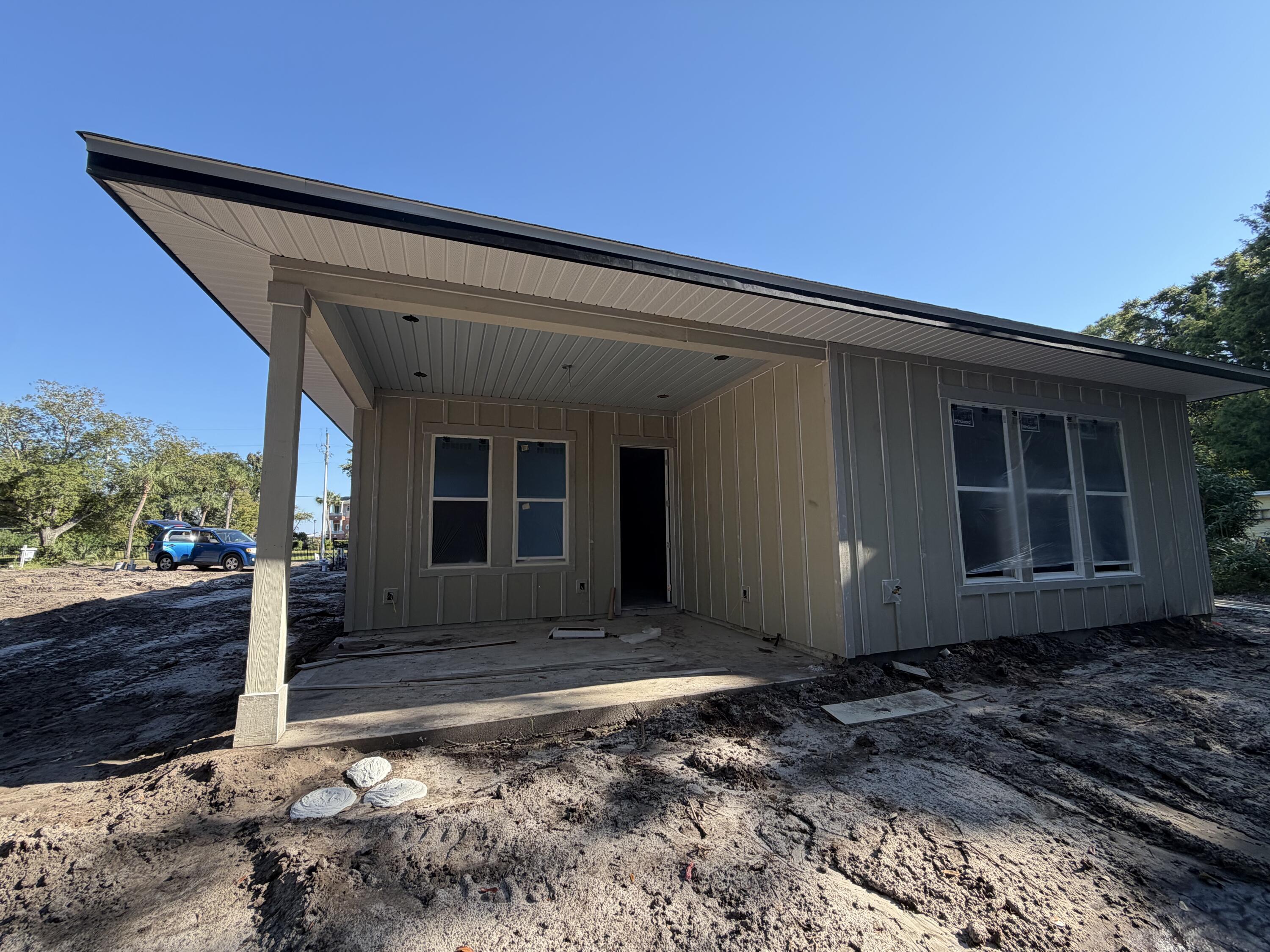 Home under construction with a wide covered porch and unfinished muddy yard.