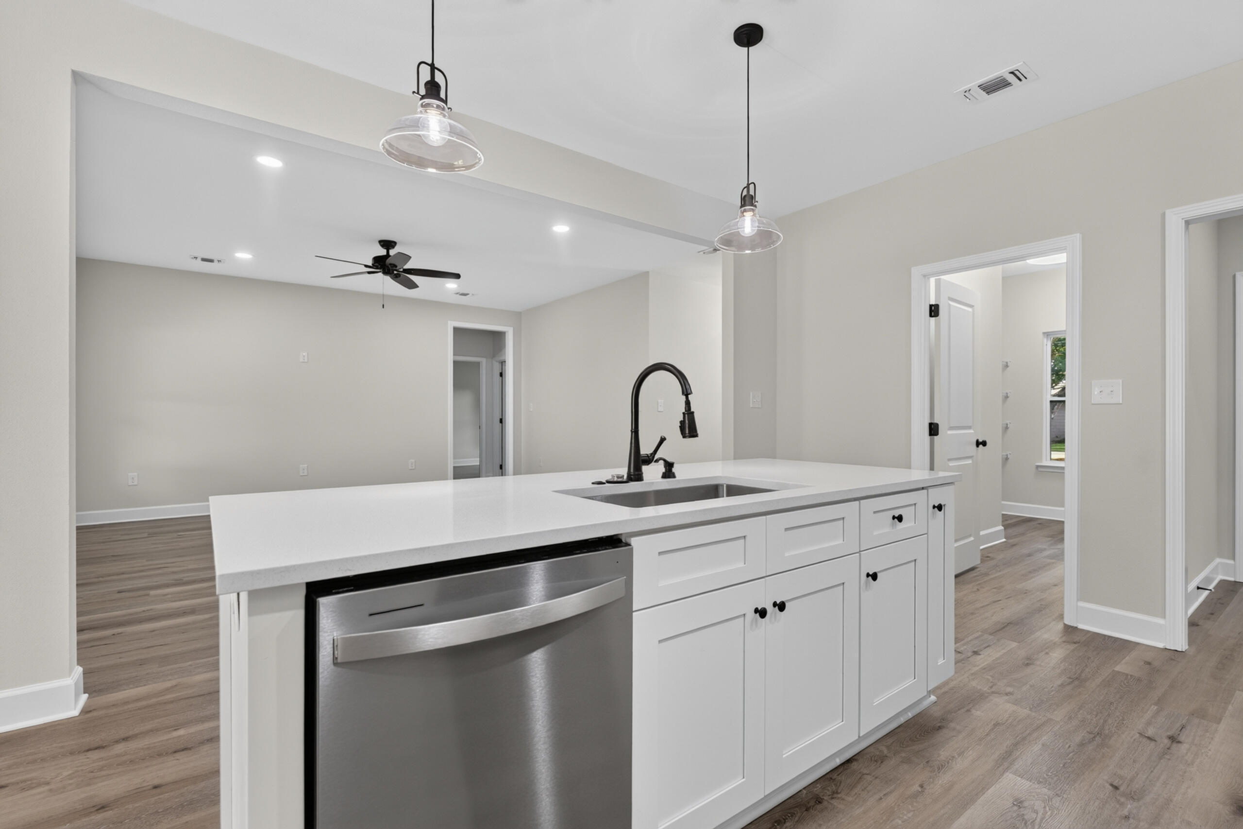 Empty kitchen with a large white island, black faucet, stainless steel dishwasher, and wood-look floors.