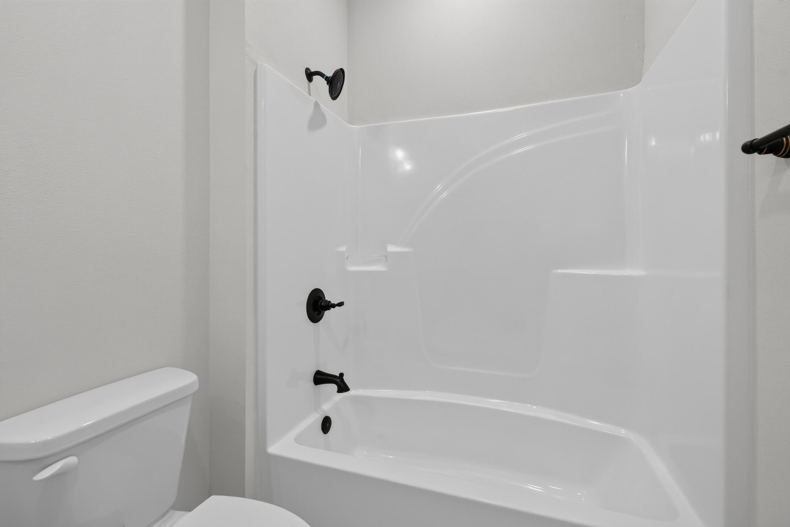 Bathroom with a white tub and shower surround and black fixtures beside a toilet.
