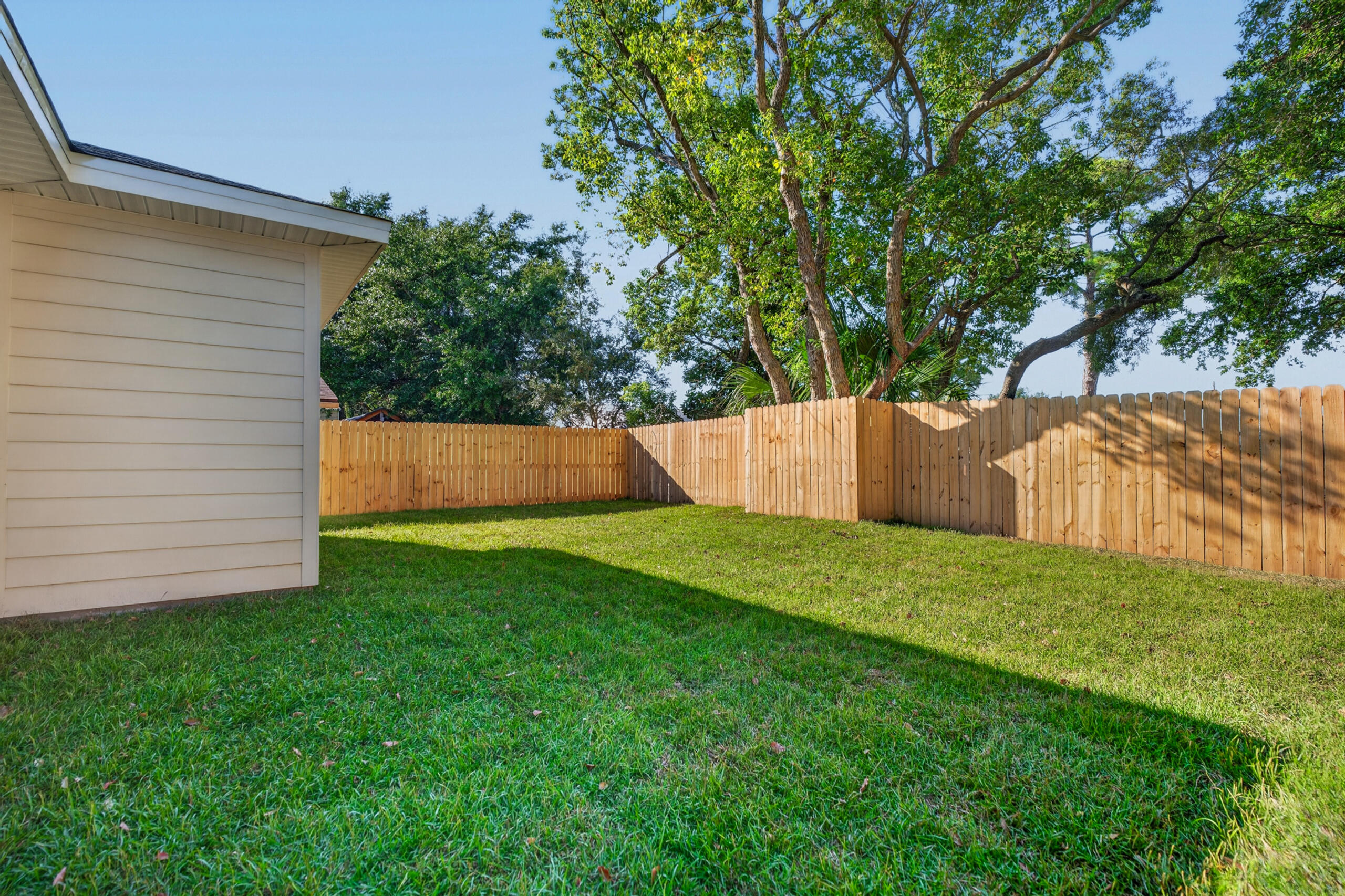 Fenced backyard with a green lawn, wooden privacy fence, and mature shade trees.