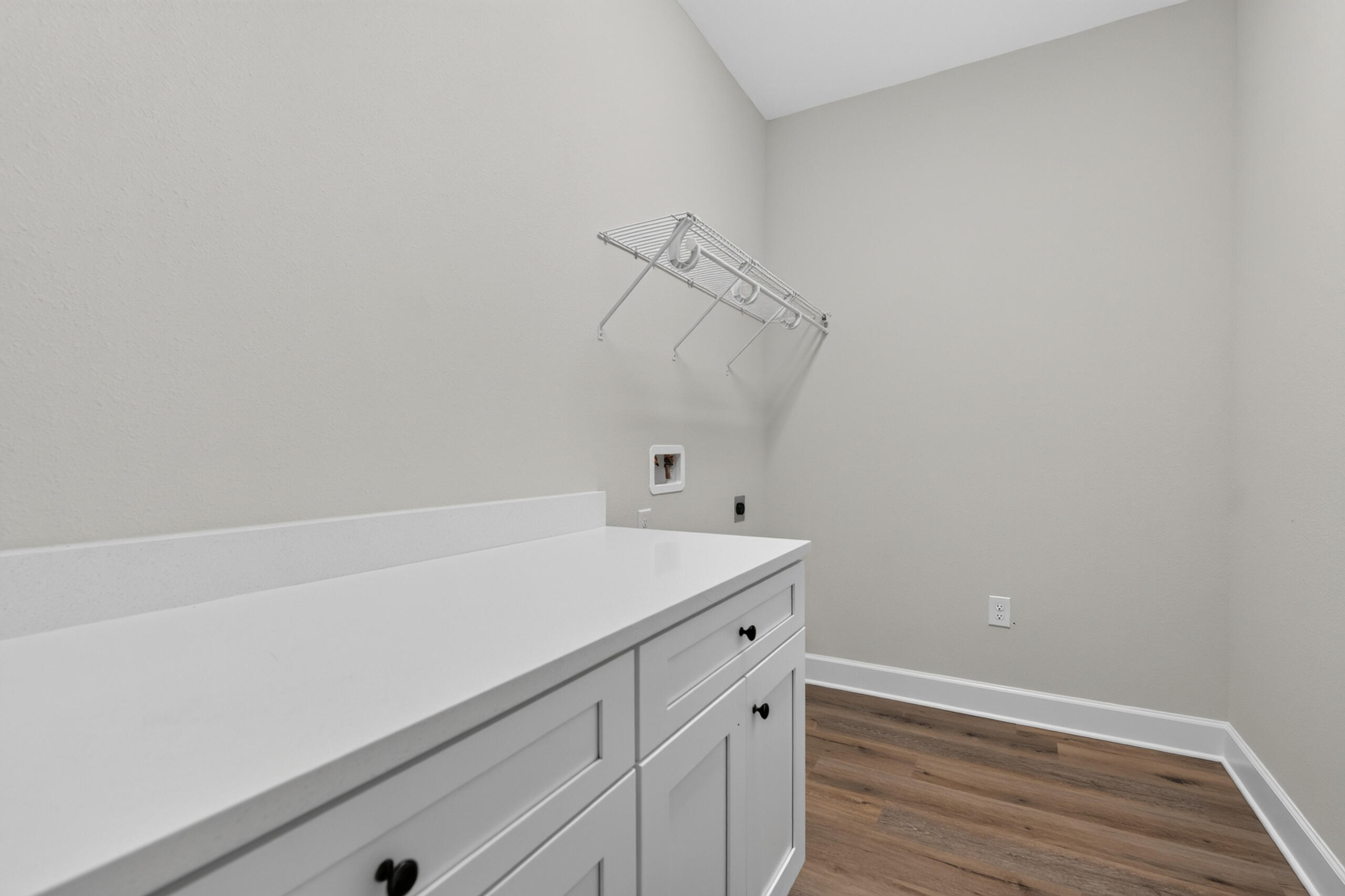 Laundry room with white cabinets, a long countertop, wall-mounted drying rack, and wood-look flooring.