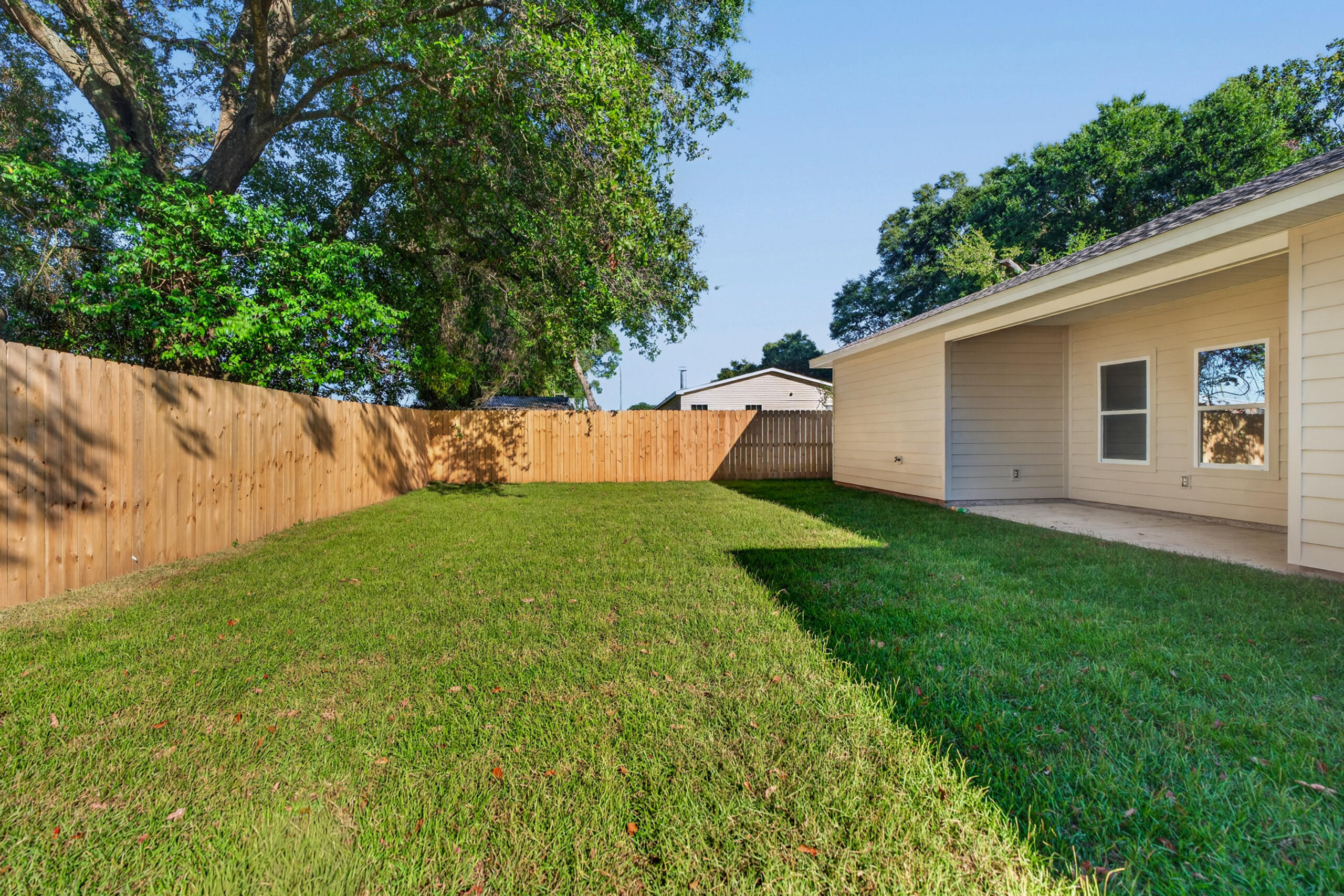 Grassy backyard enclosed by a wooden privacy fence, with mature trees and a covered patio.