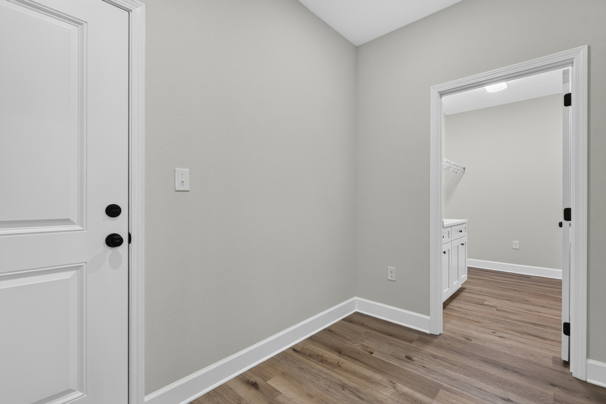 Entryway with a white paneled door and wood-look flooring, opening to a room with white cabinetry.